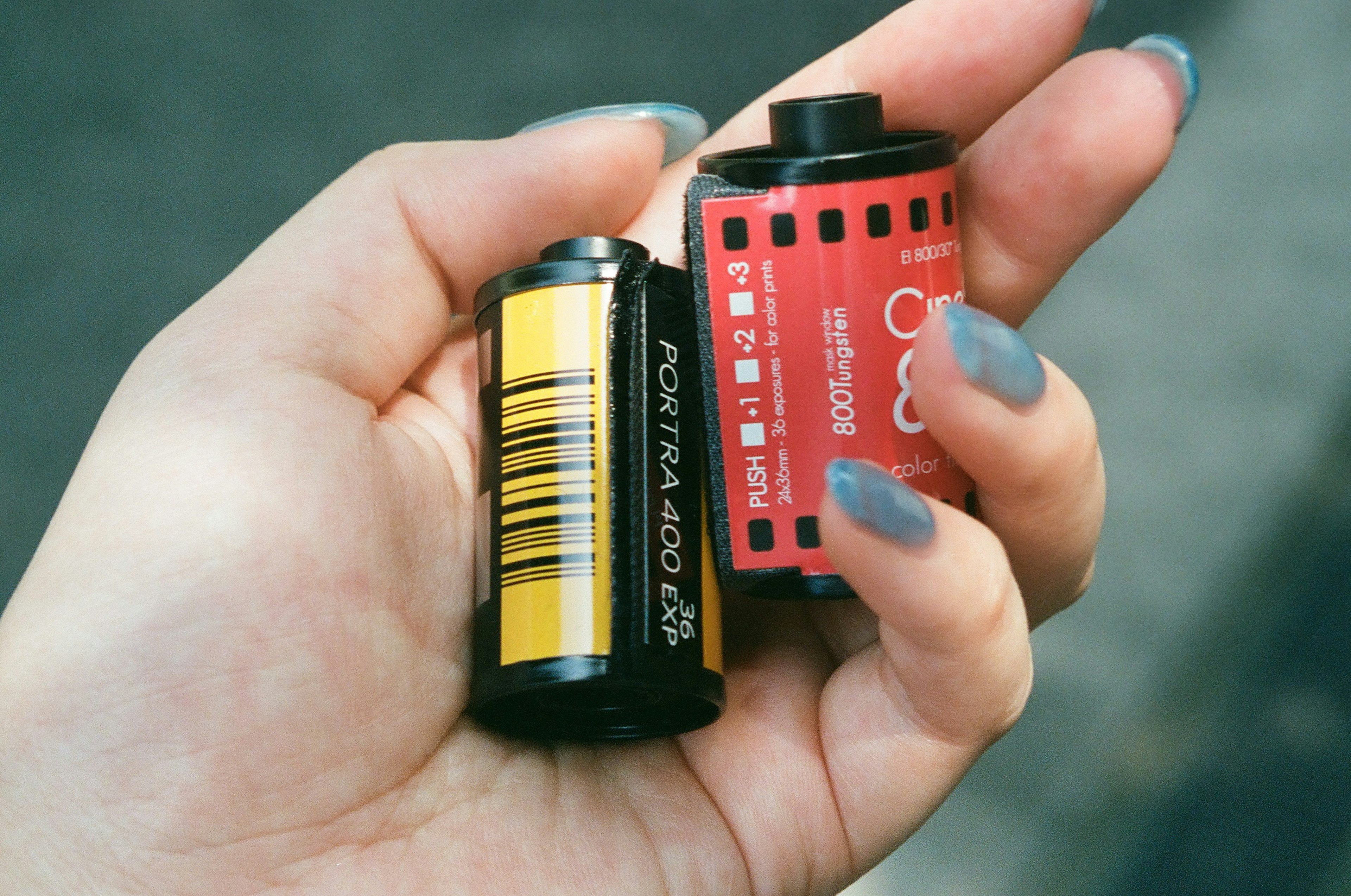 Mano sosteniendo dos rollos de película uno negro y amarillo y uno rojo