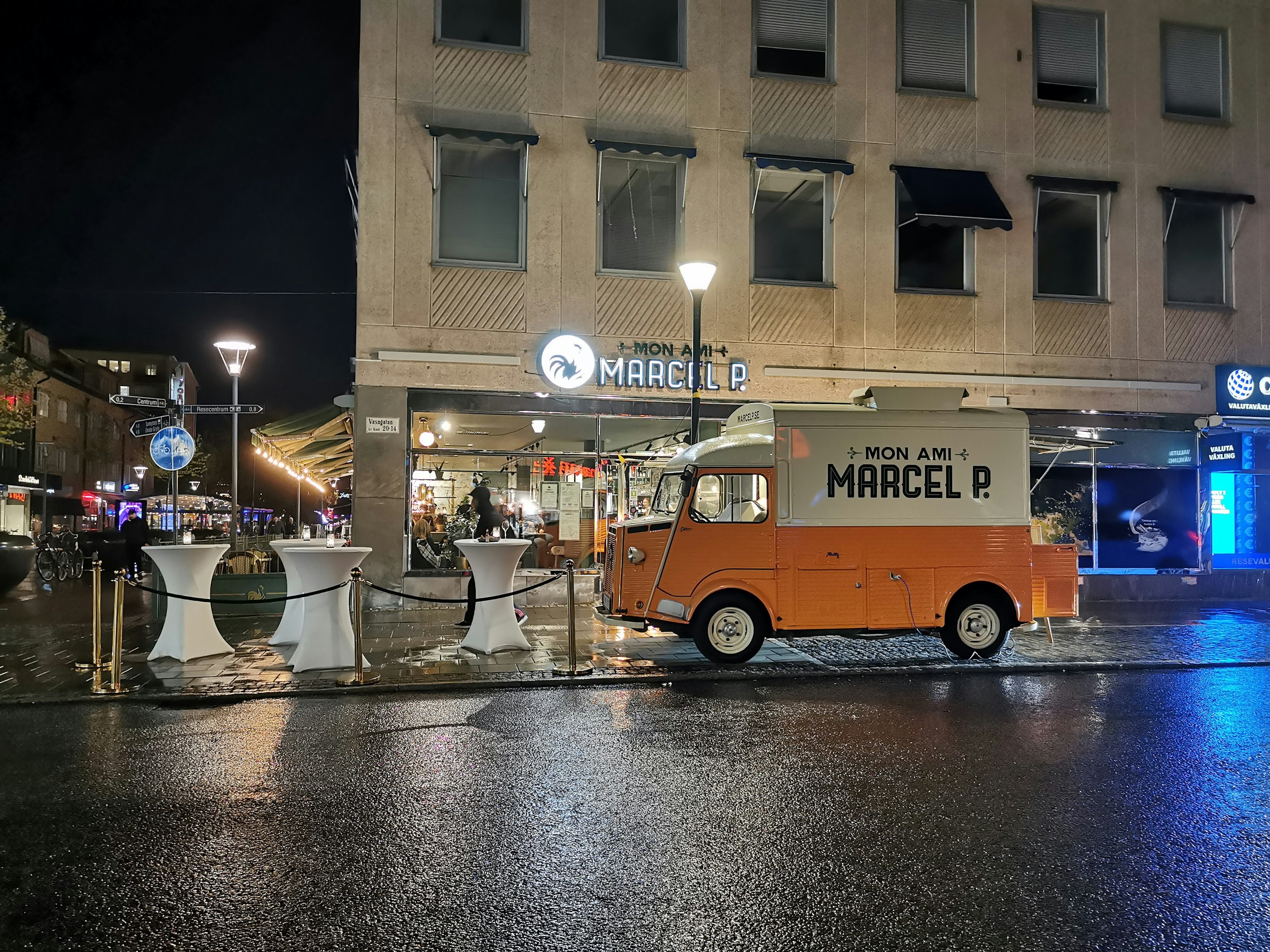 Camión de comida naranja estacionado de noche cerca del restaurante Marcel