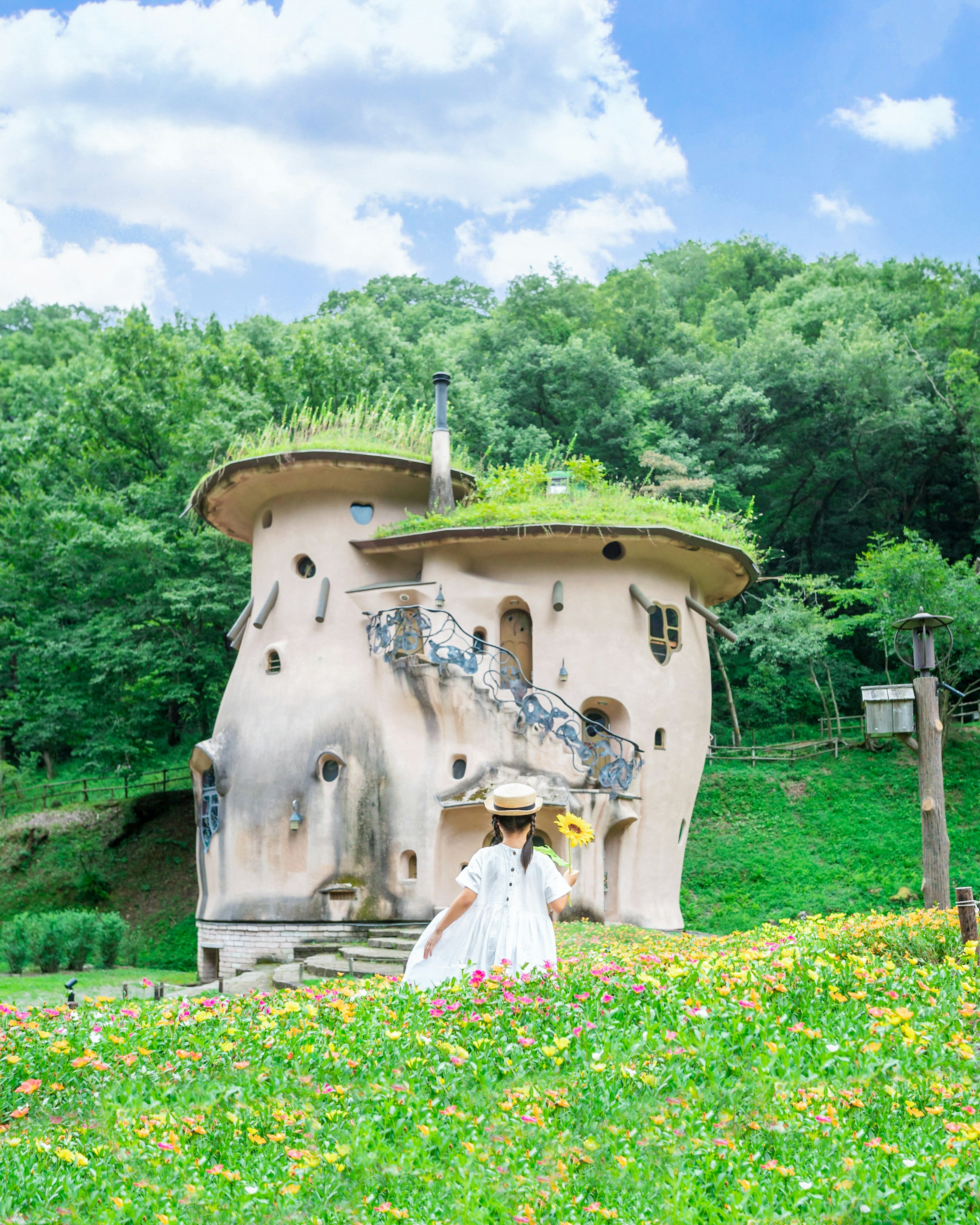 緑に囲まれたユニークなデザインの家と花を持つ女性