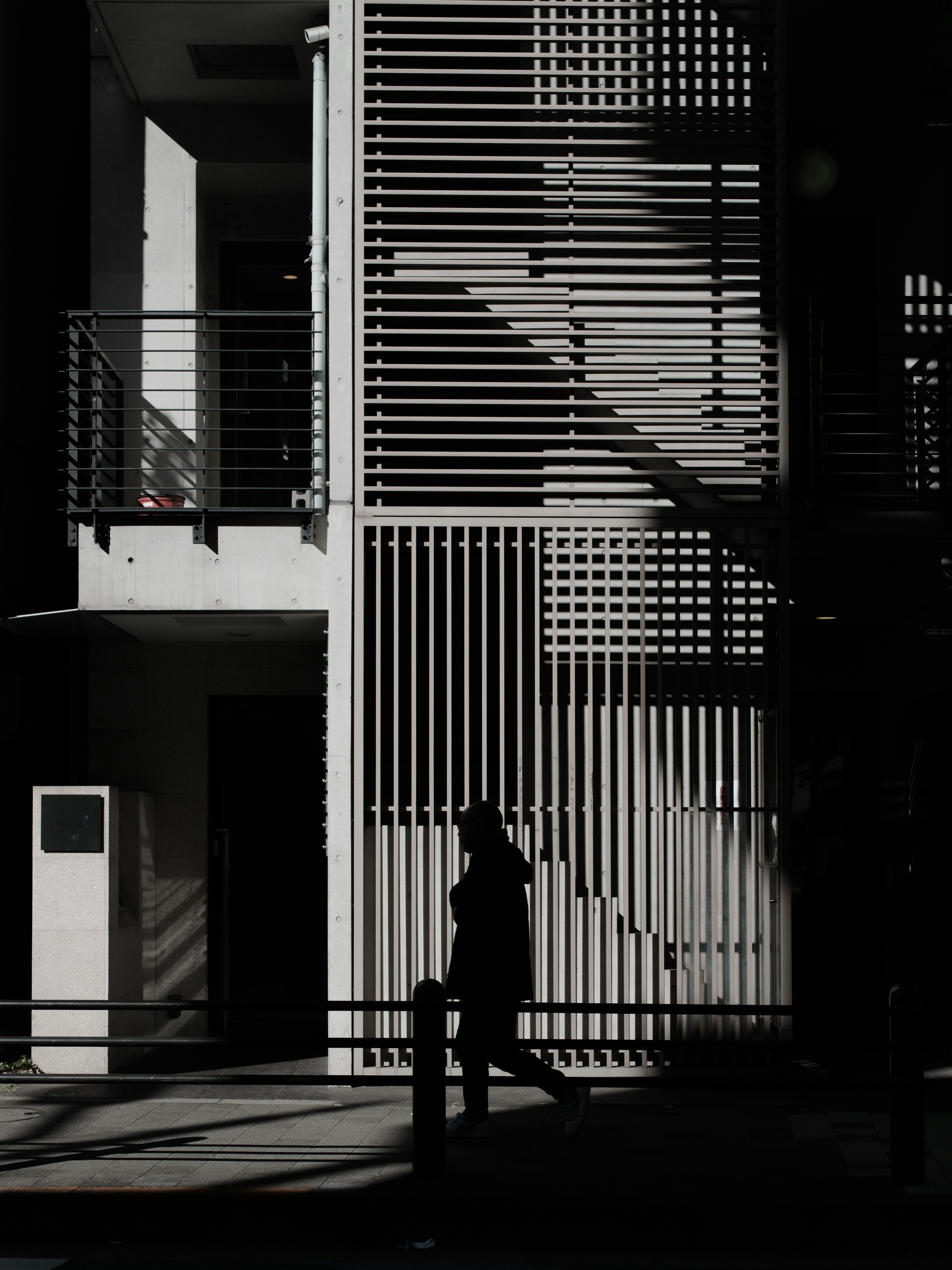 Silhouette einer Person, die neben einem gestreiften Gebäude mit Schatten geht