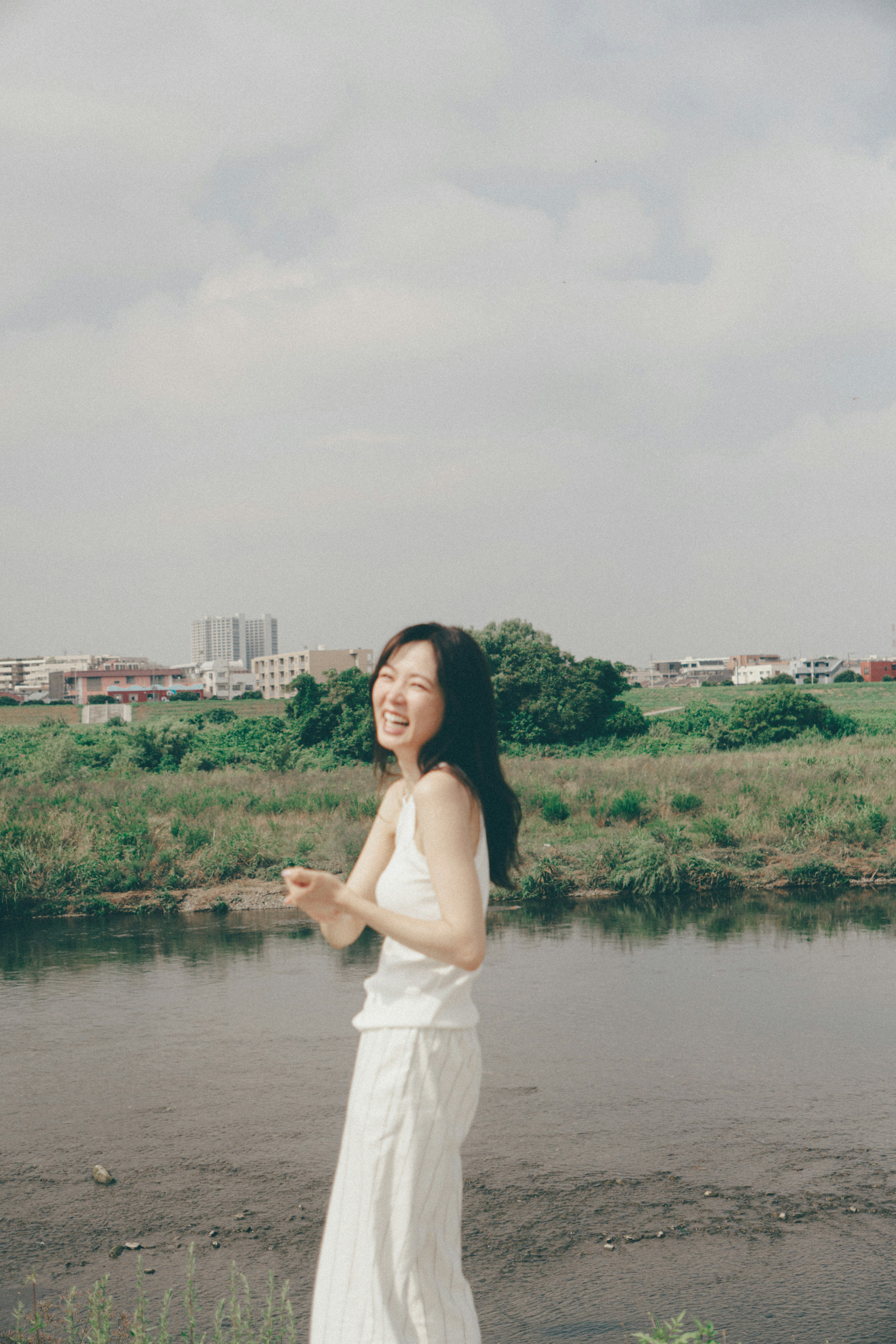 A woman in a white dress standing by the river smiling