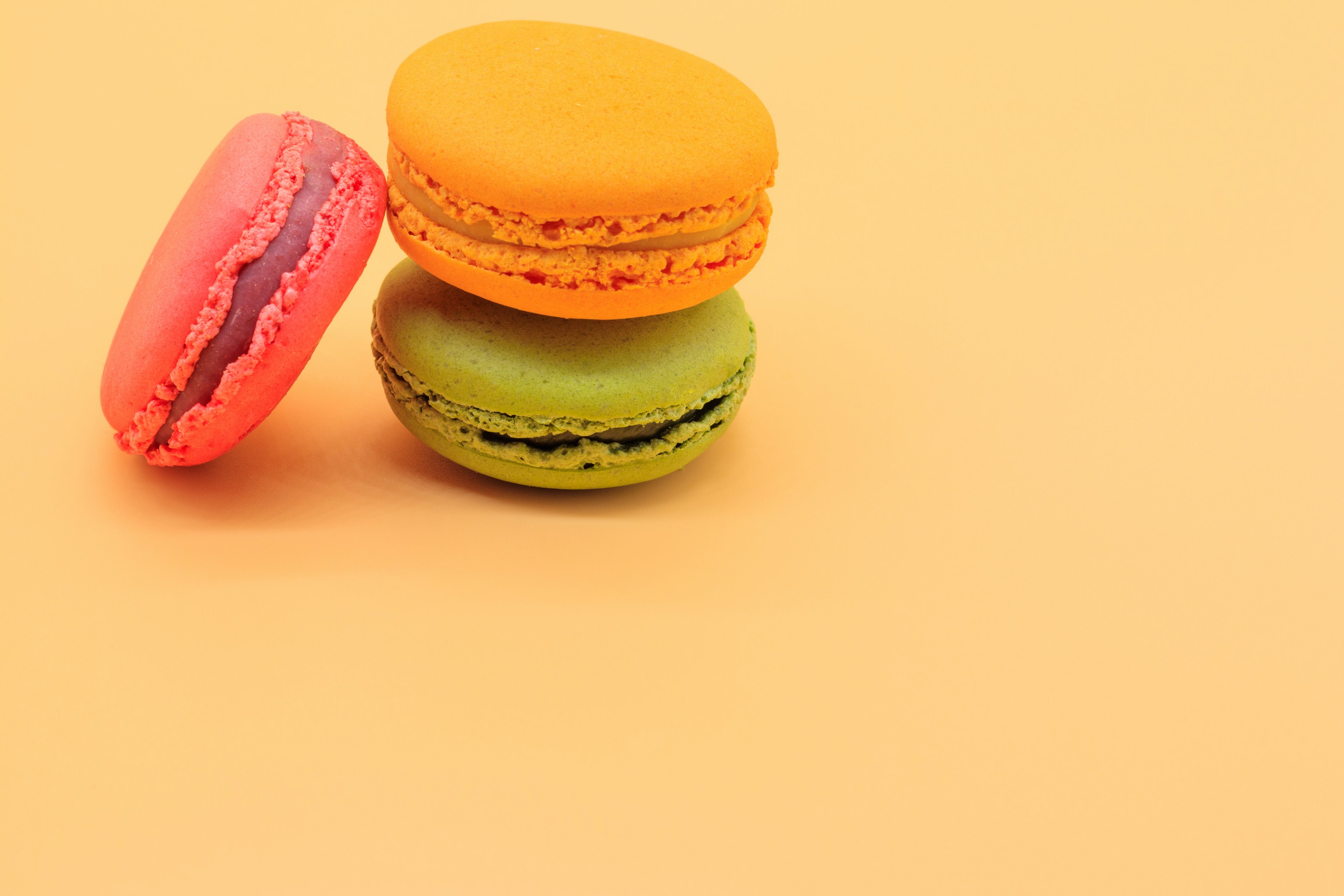 Tres macarons coloridos apilados sobre un fondo naranja vibrante