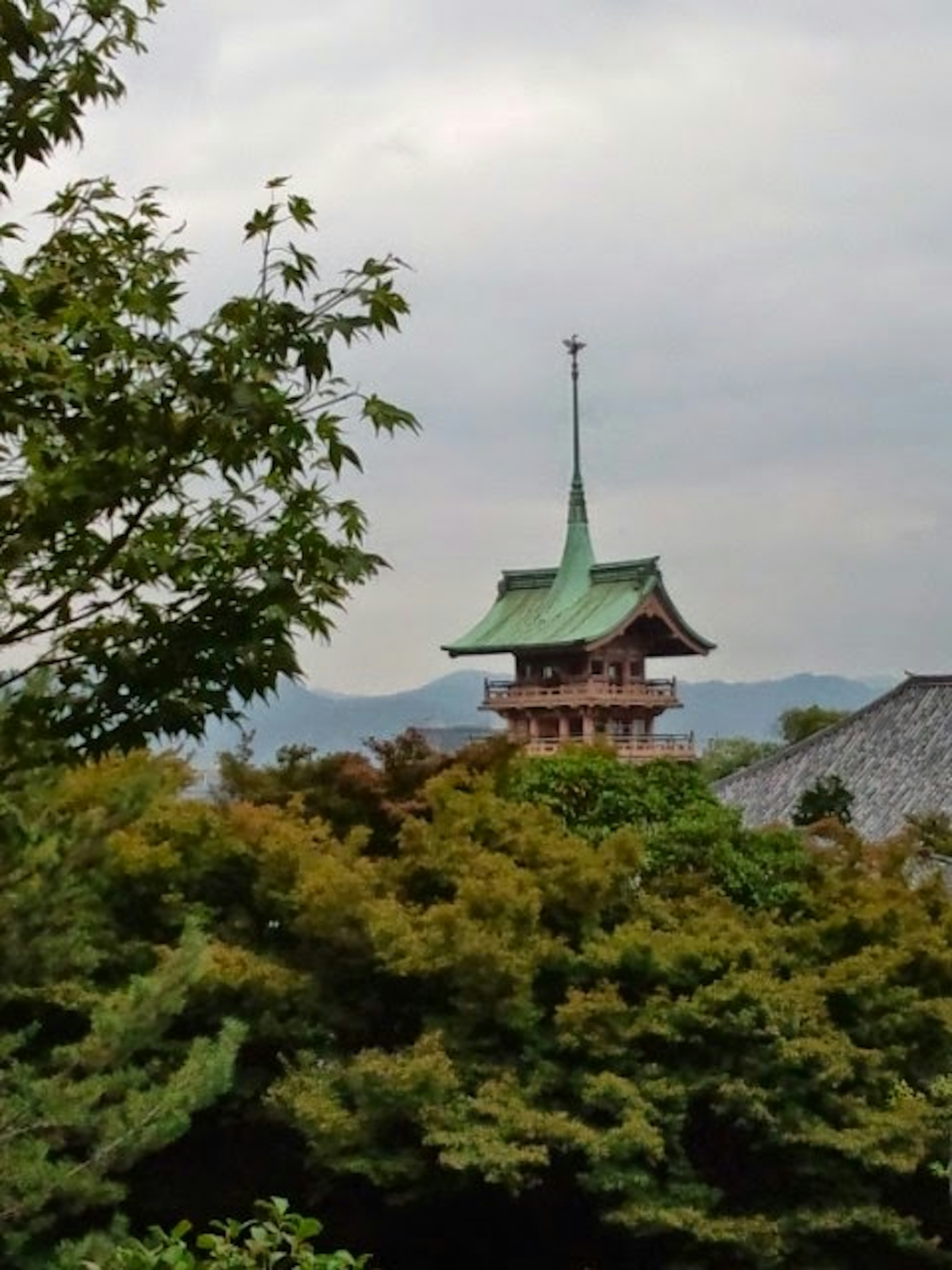 Torre japonesa tradicional con techo verde visible entre los árboles