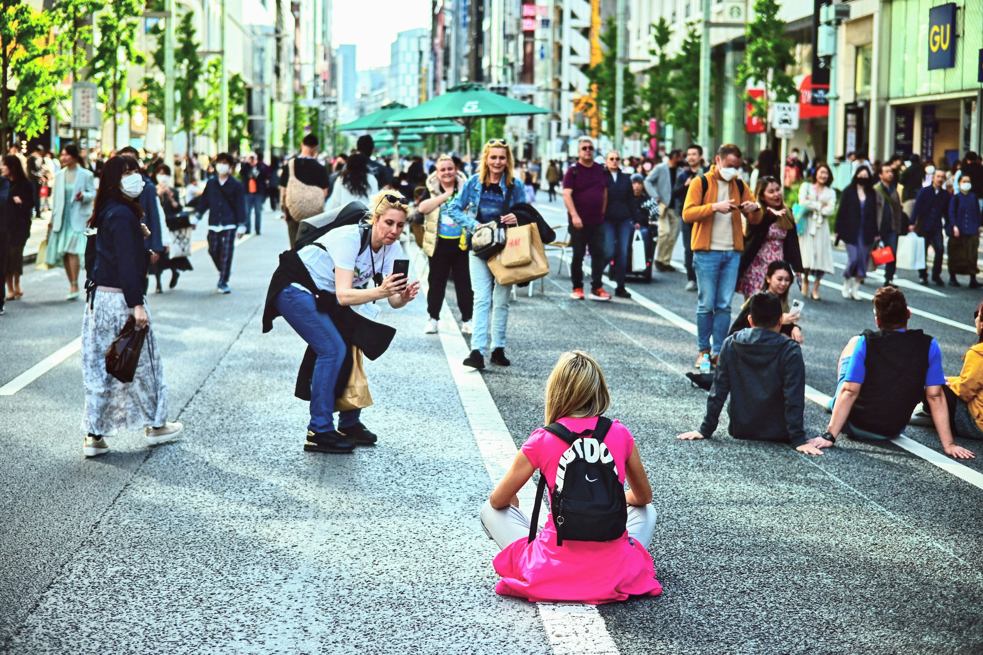 Crowd in a busy street with people posing and a woman sitting