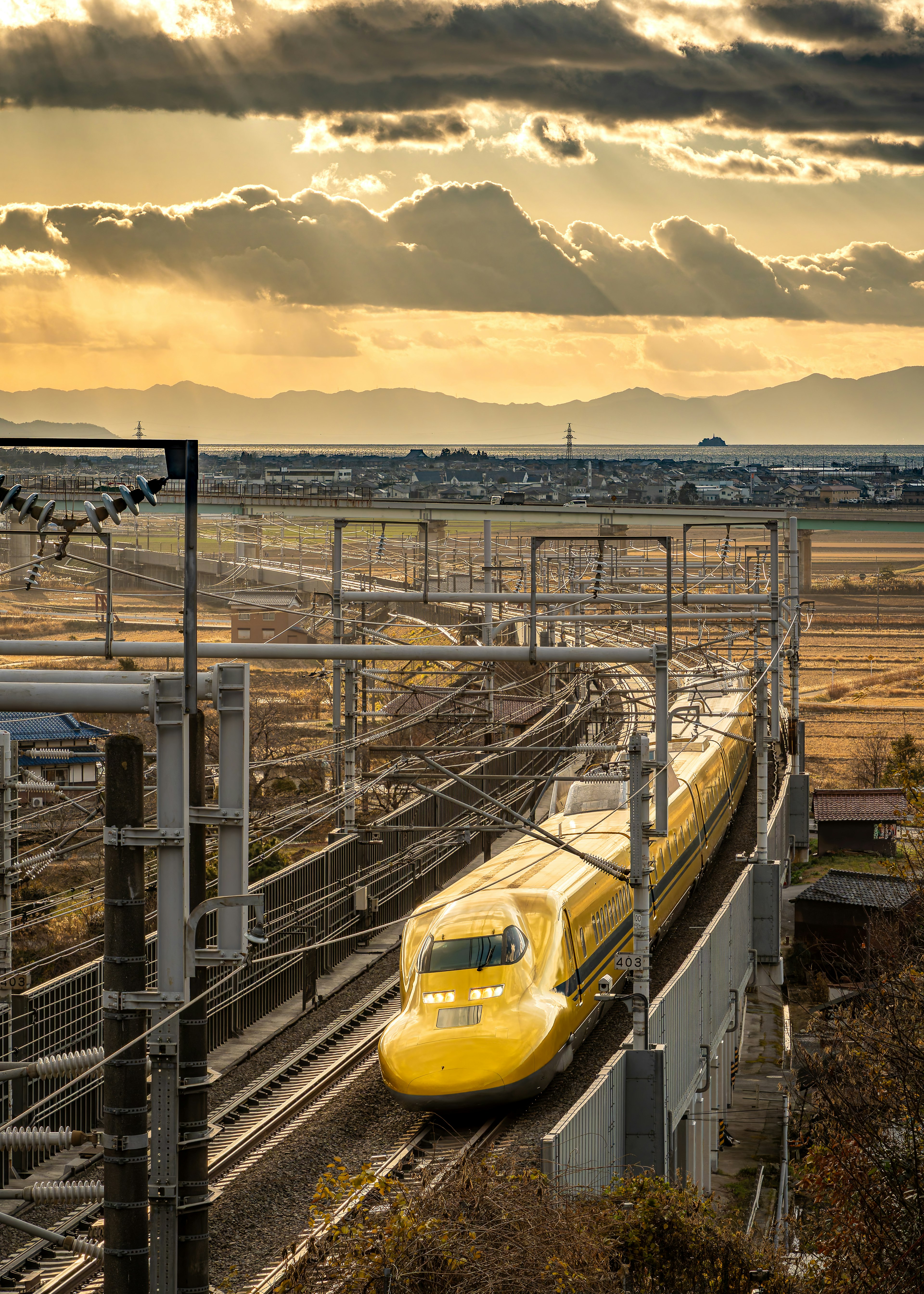 Kereta Shinkansen kuning melintasi pemandangan matahari terbenam