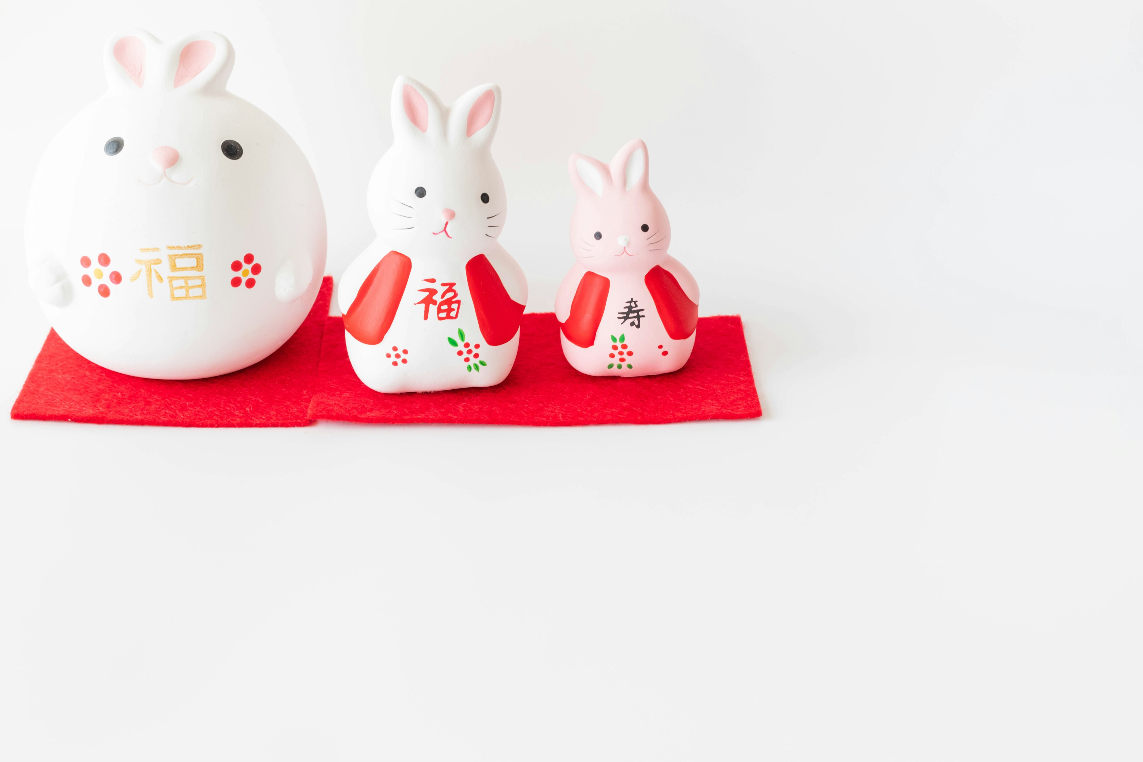 Trois figurines de lapins disposées sur un tissu rouge sur fond blanc