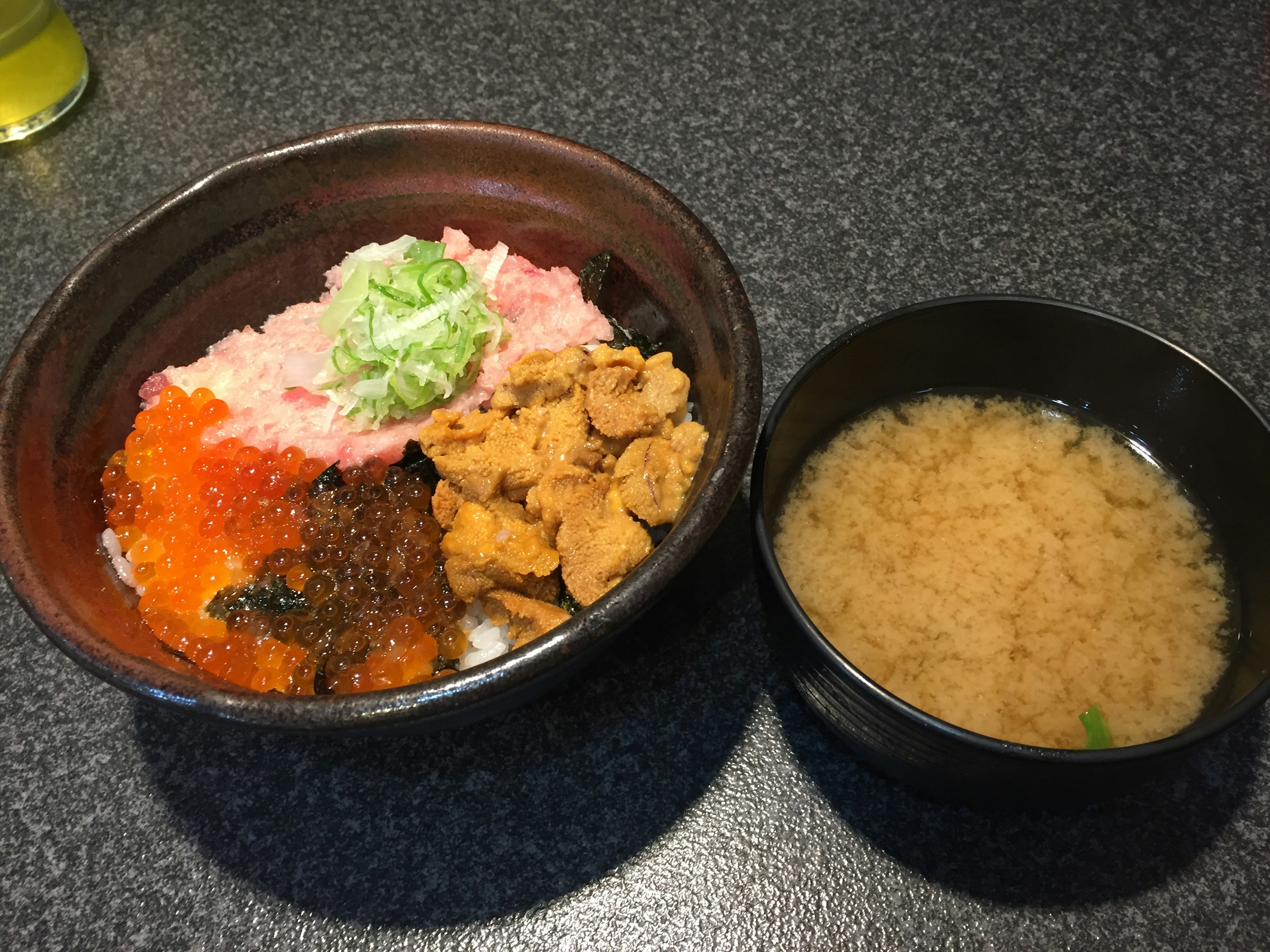 Eine Schüssel Seafood Donburi mit Miso-Suppe auf einem dunklen Tisch