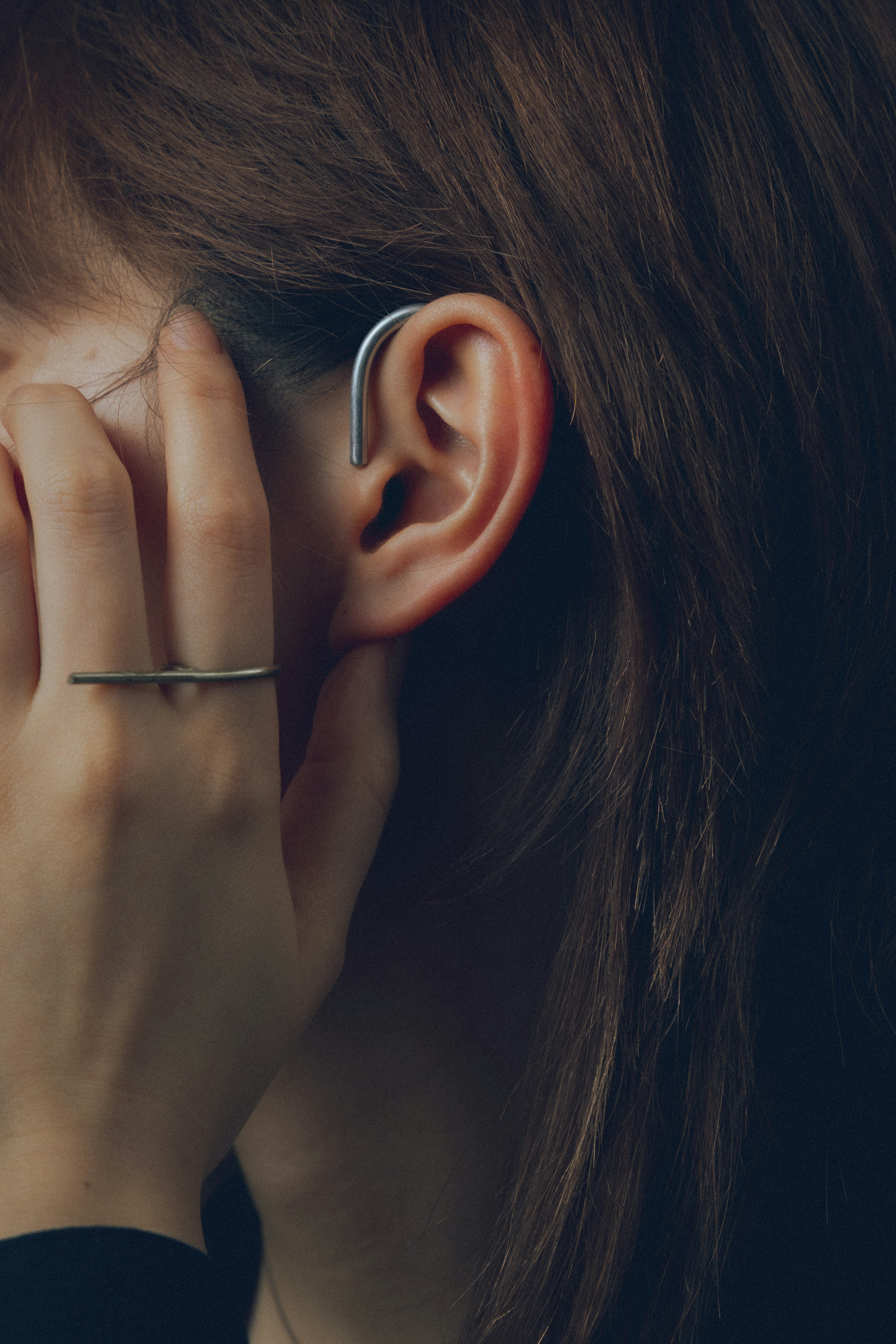 Profilo laterale di una donna con la mano sull'orecchio capelli castani e orecchino elegante visibile