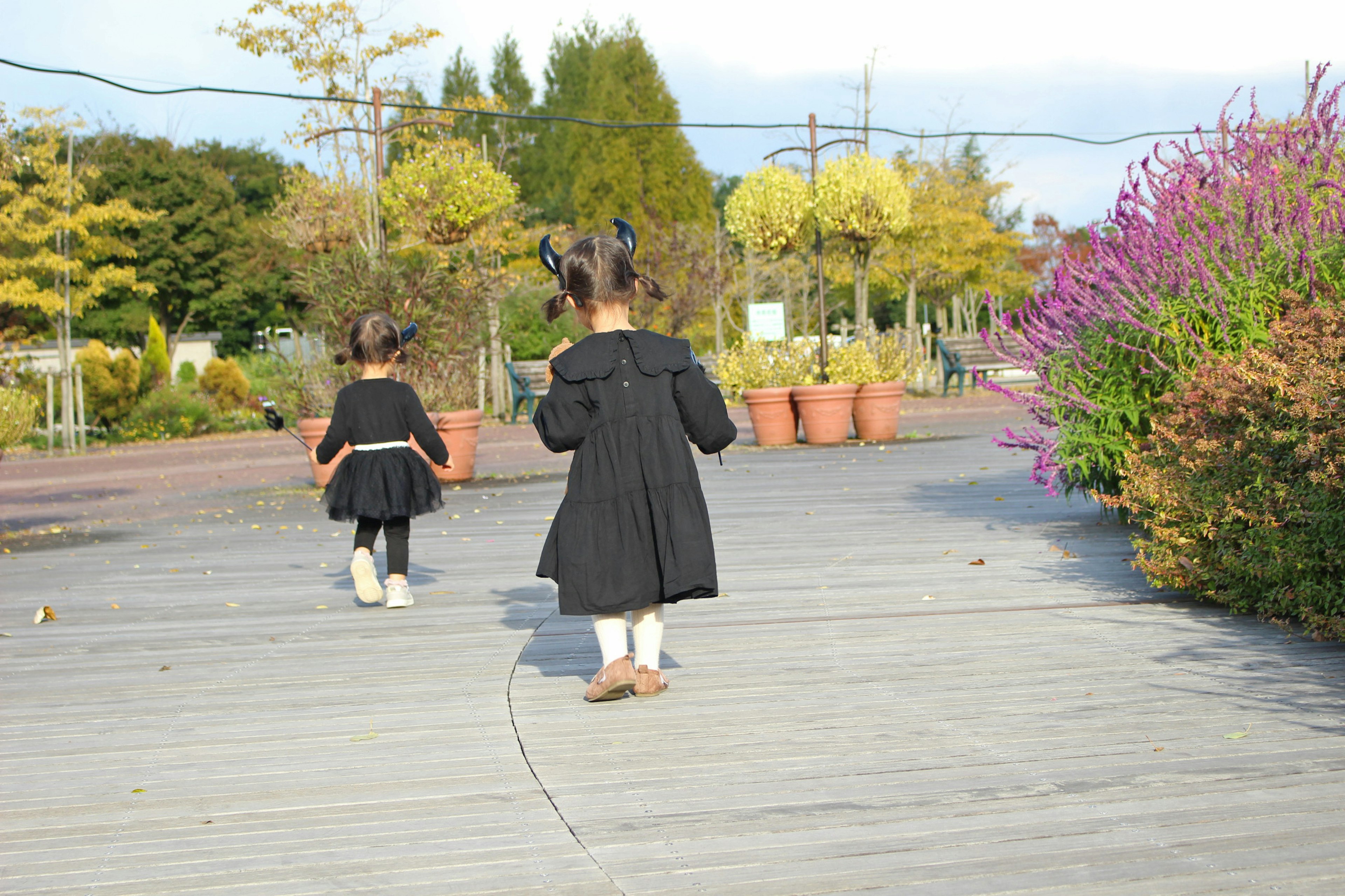 Deux enfants marchant sur une terrasse en bois dans un parc entouré de plantes et de fleurs