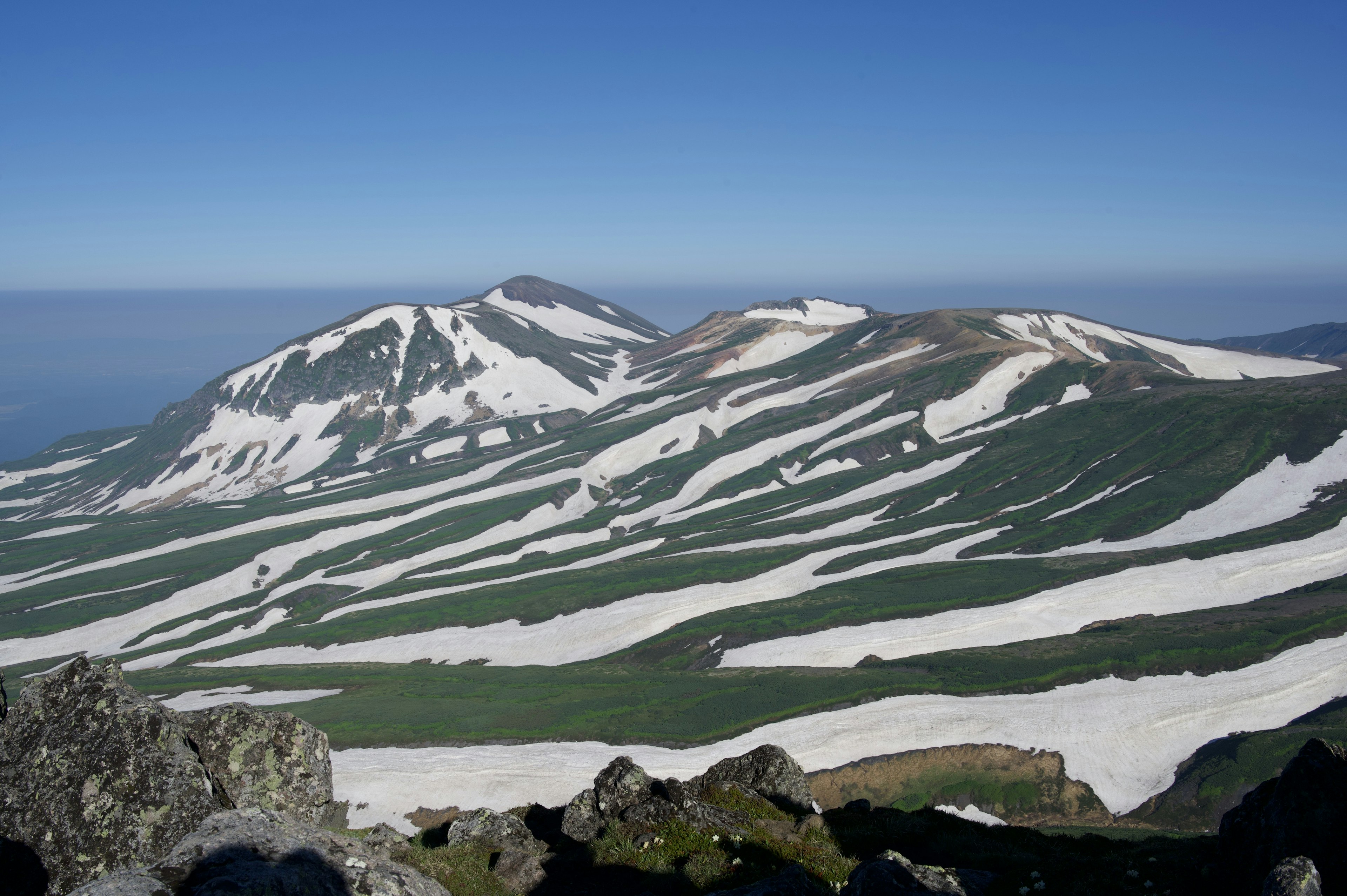 Montañas cubiertas de nieve con laderas verdes y cielo azul claro