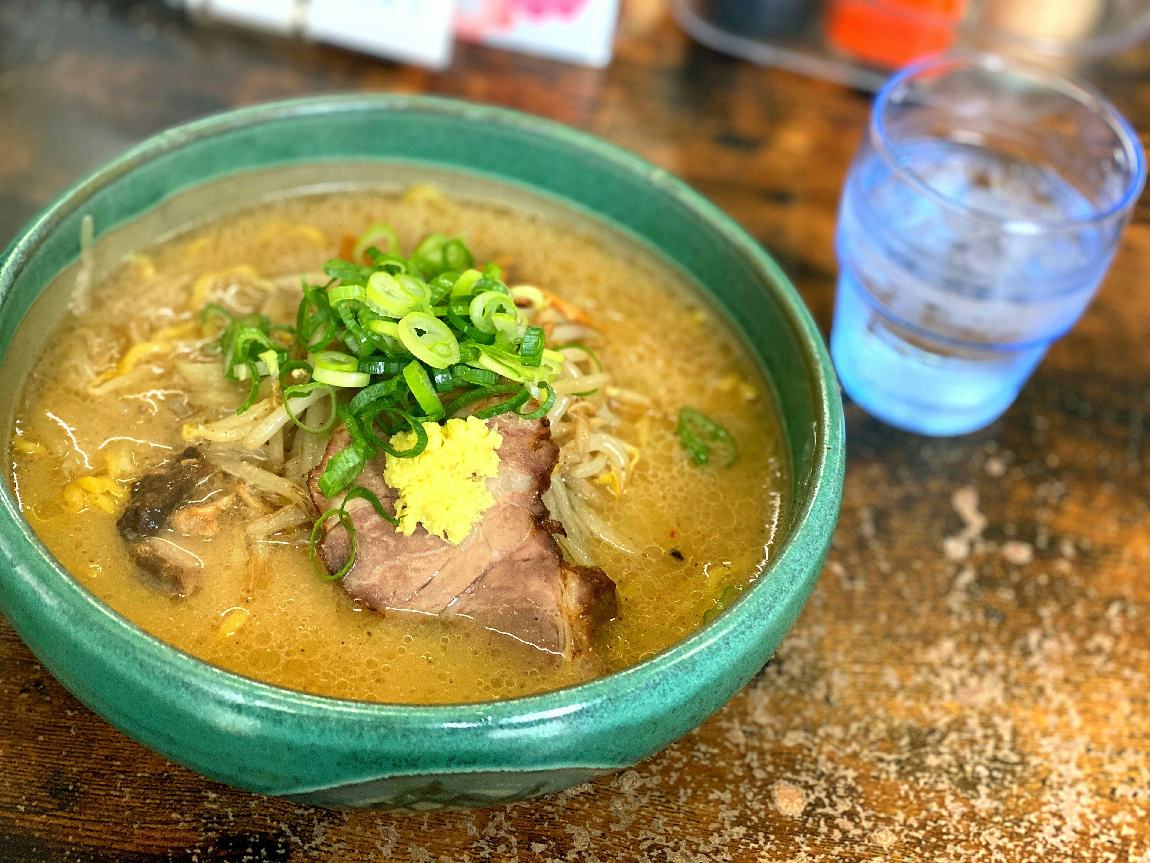 Ramen soup in a green bowl topped with green onions and ginger