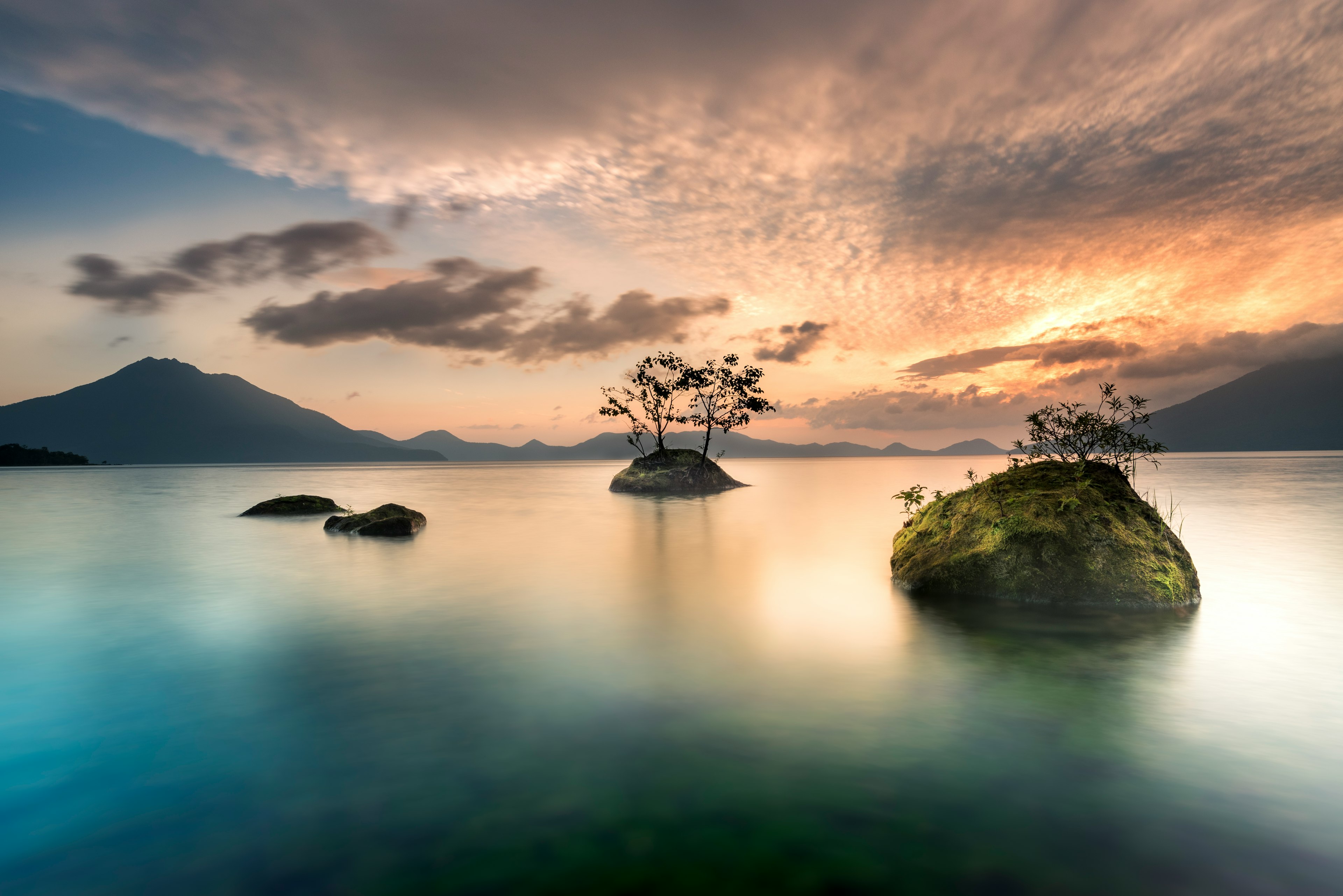 Ruhige Seenlandschaft mit kleiner Insel und silhouettierten Bäumen vor einem schönen Sonnenuntergangshimmel