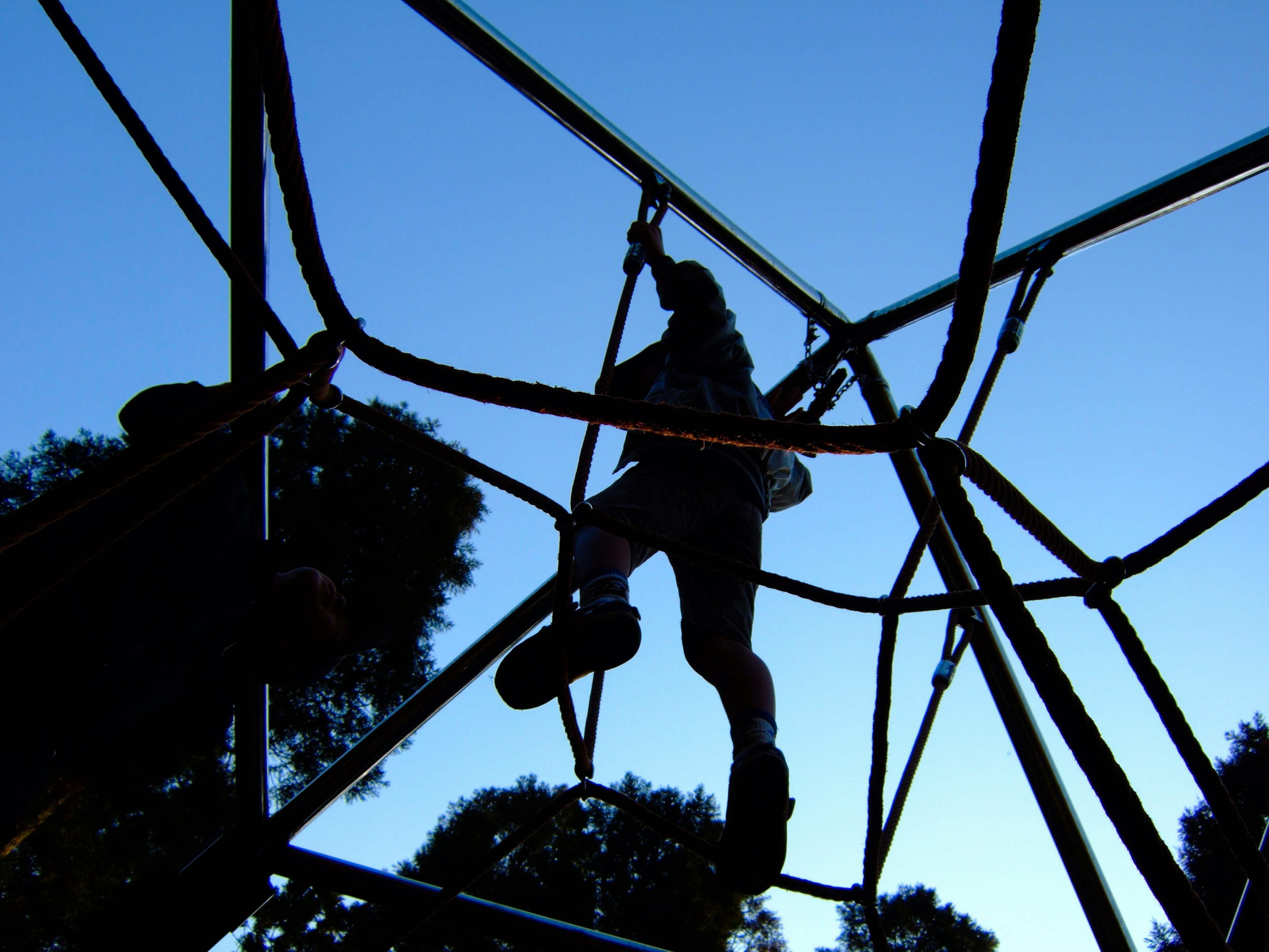 Silhouette d'un enfant jouant sur une structure d'escalade sous un ciel bleu