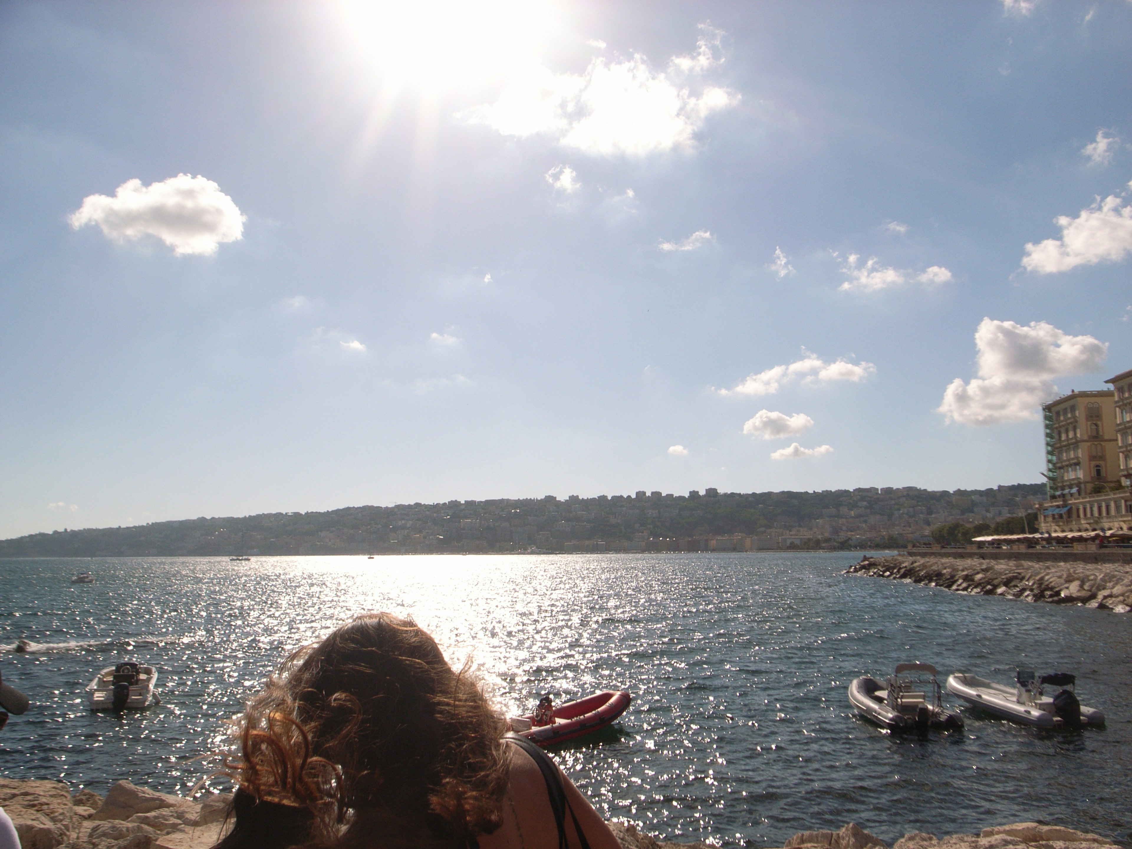 Szenen von einer Küste mit Menschen in der Sonne und Booten im Wasser