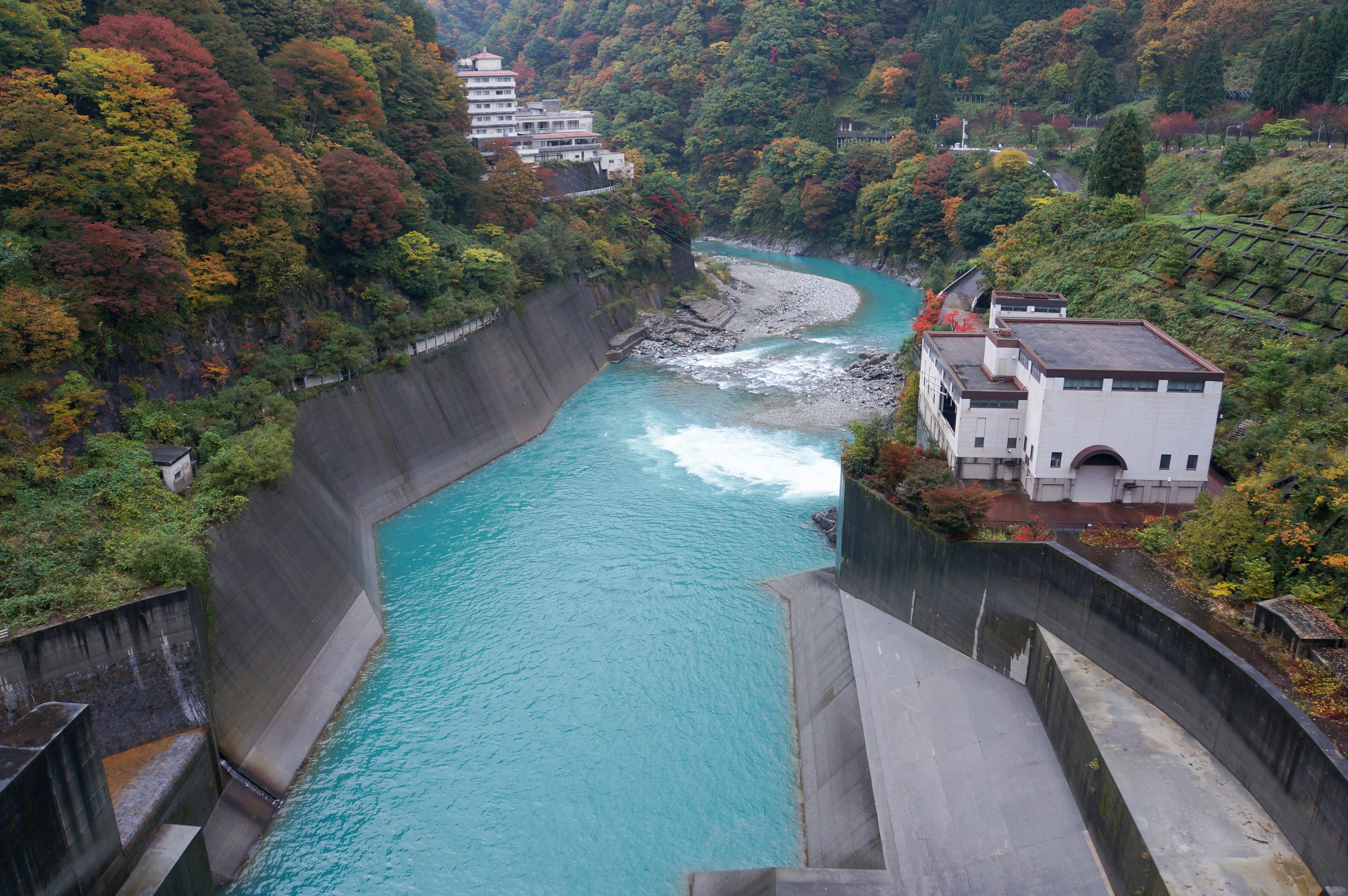 Malersicher Blick auf einen türkisfarbenen Fluss umgeben von Herbstlaub und einem Damm