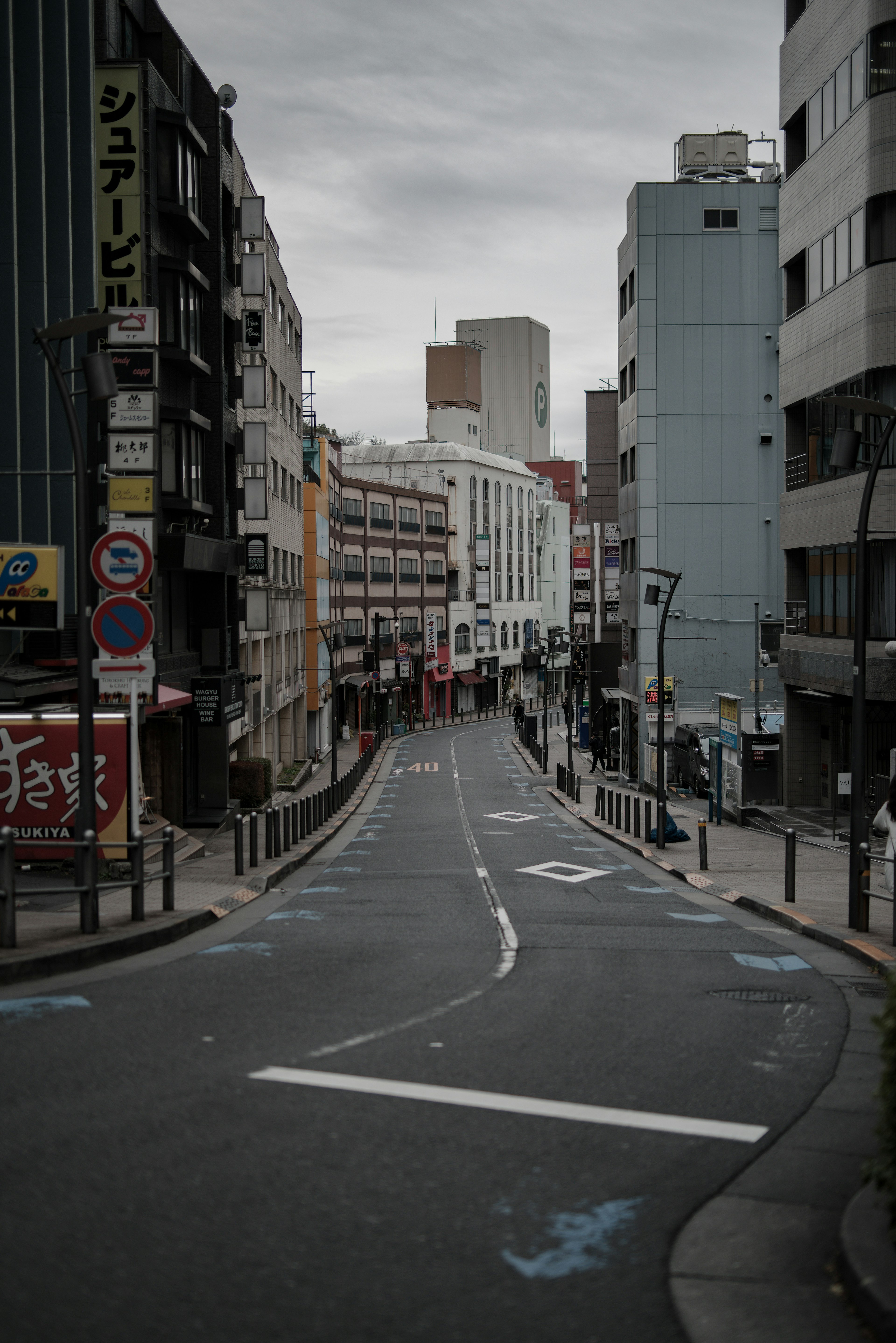 Rue urbaine calme avec peu de piétons, ciel gris, bordée de bâtiments