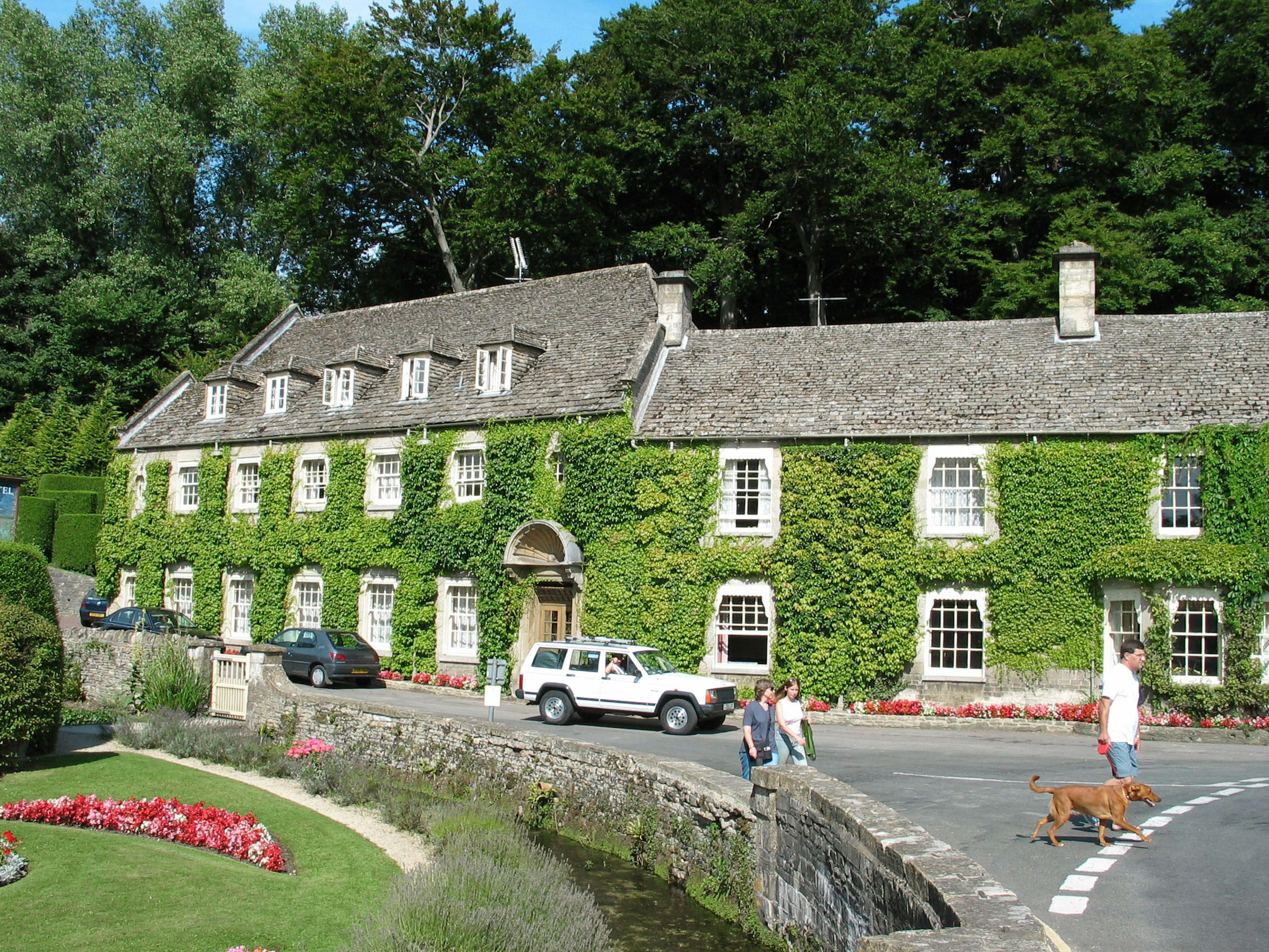 Charming stone house covered in green ivy with a flowerbed and visitors