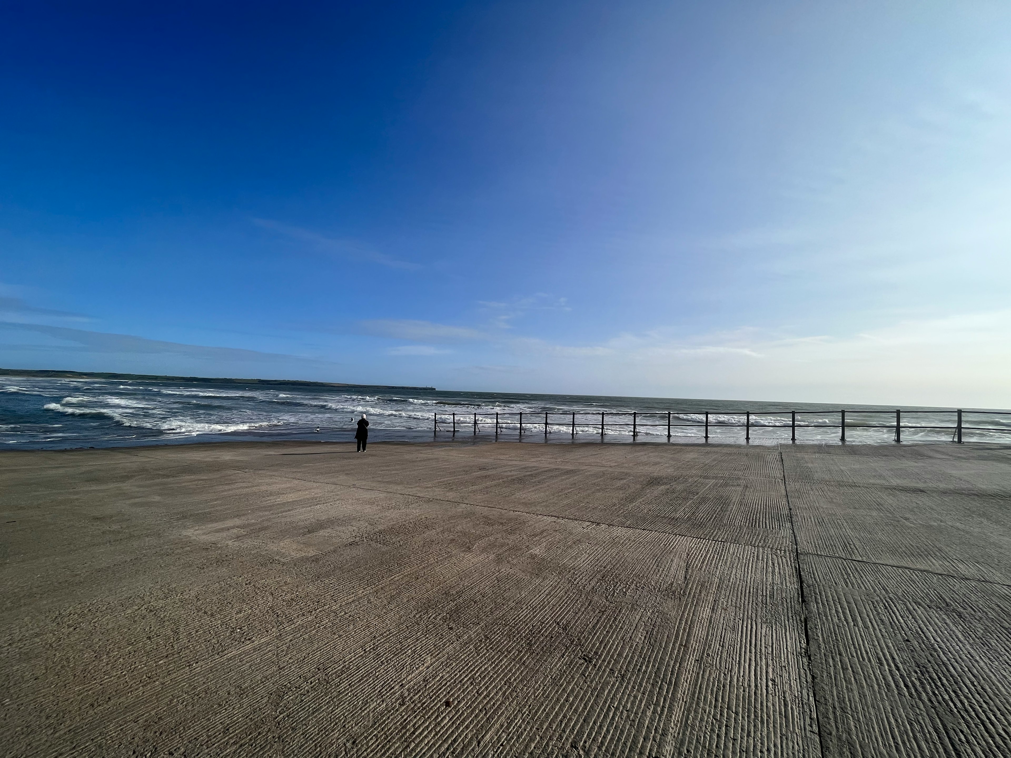 Costa de concreto con una persona de pie bajo un vasto mar y cielo azul