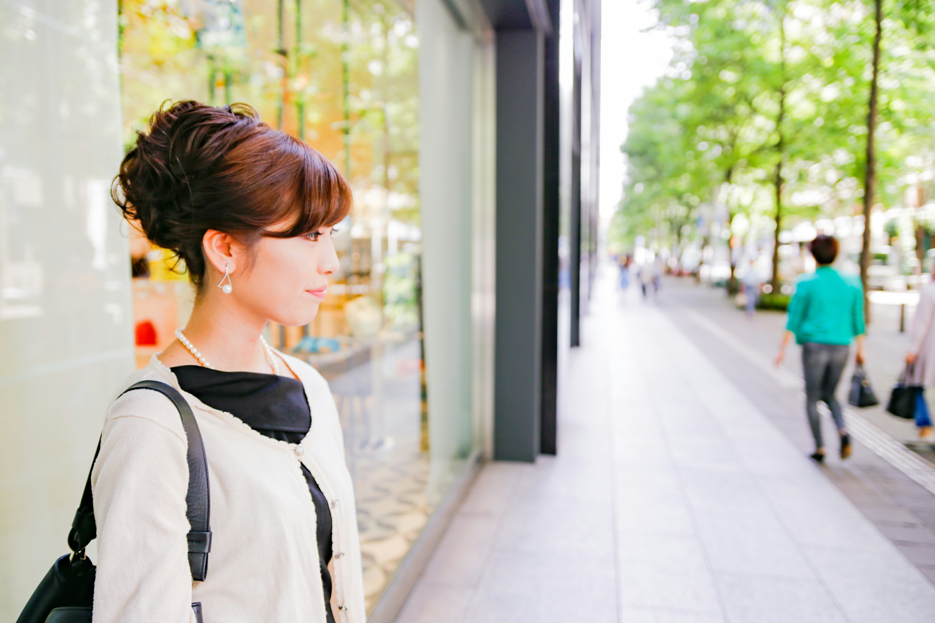 Profile view of a woman standing on the street Green trees and glass building in the background