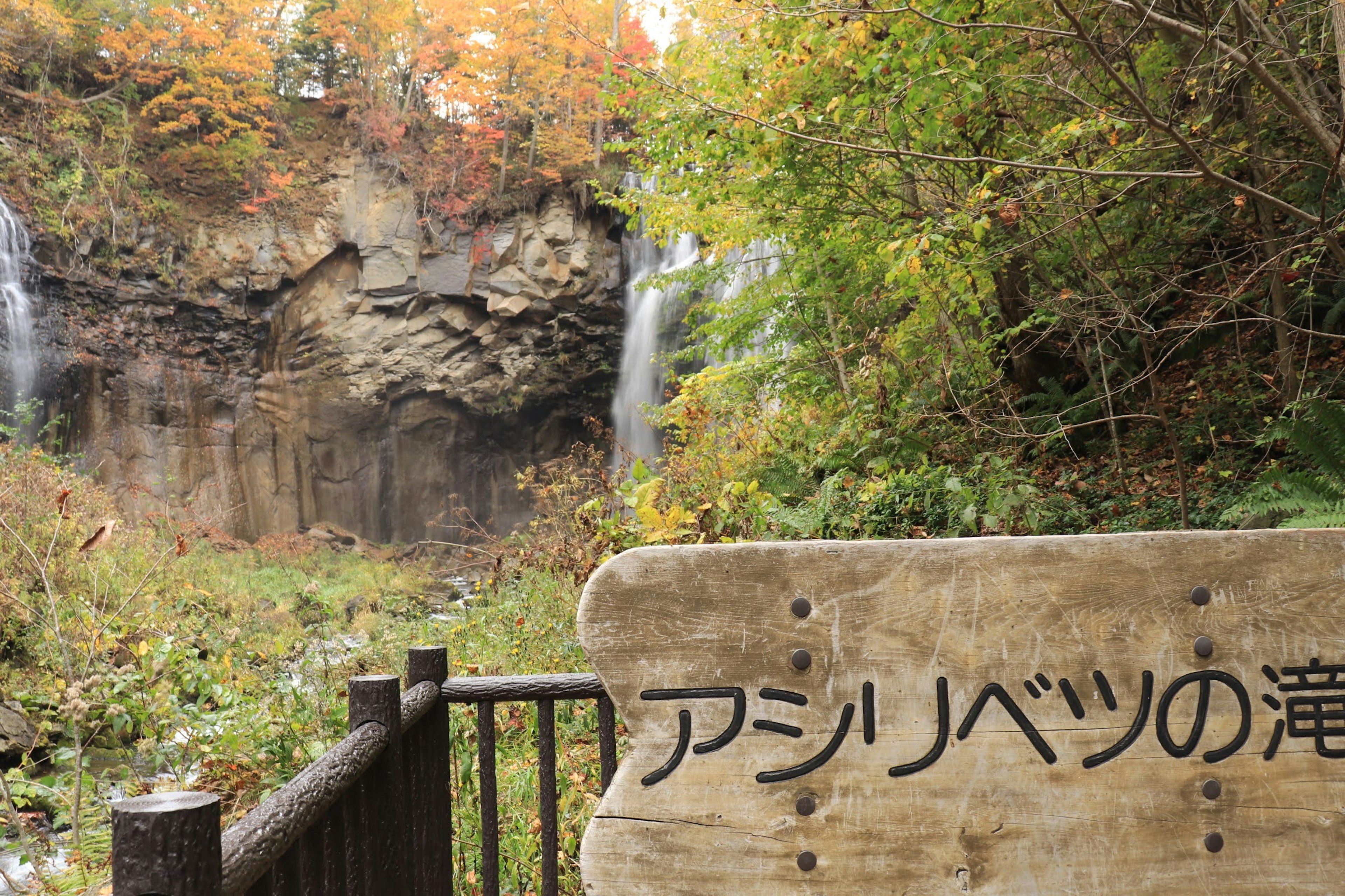 アシリベツの滝の近くにある木製の看板と秋の紅葉