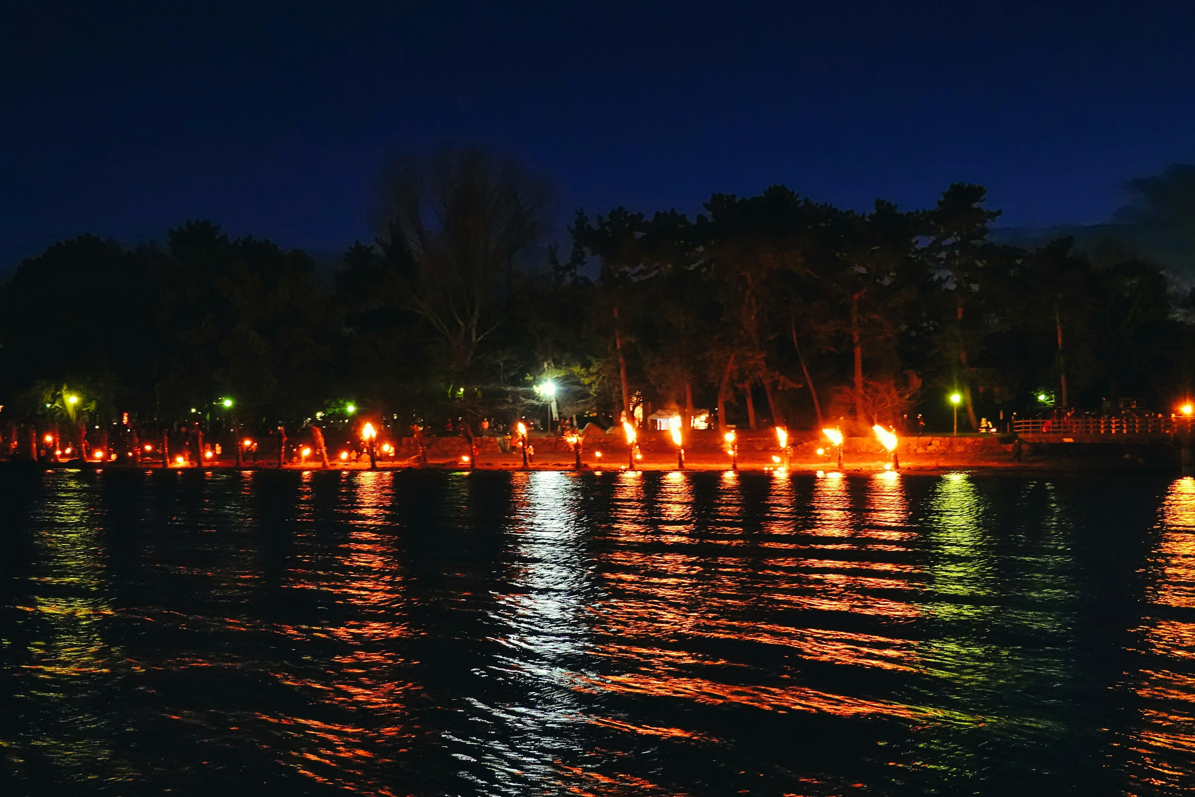 Fackeln erhellen das Ufer des Sees bei Nacht mit Reflexionen im Wasser