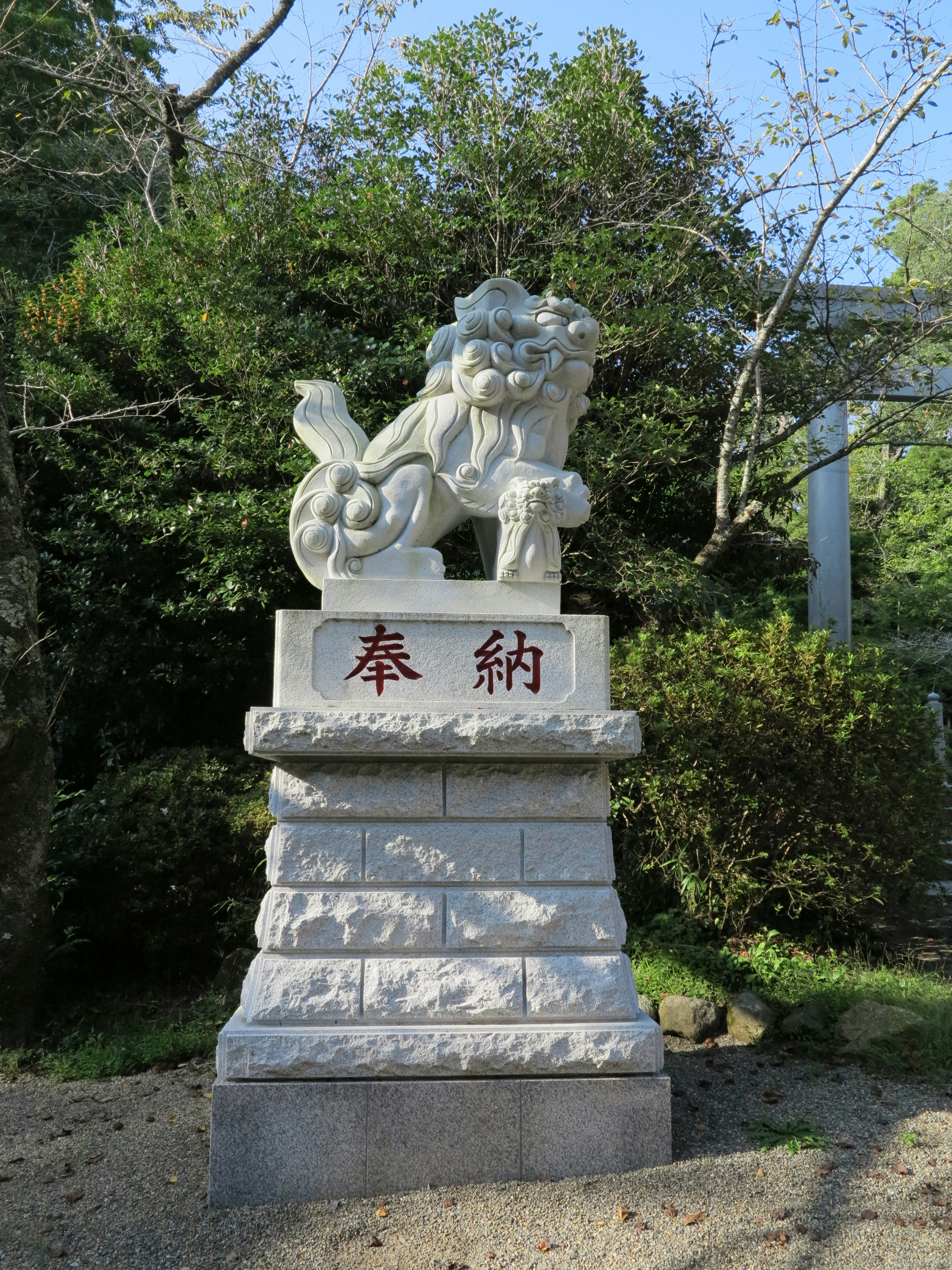 A white stone guardian lion statue at a shrine surrounded by green trees