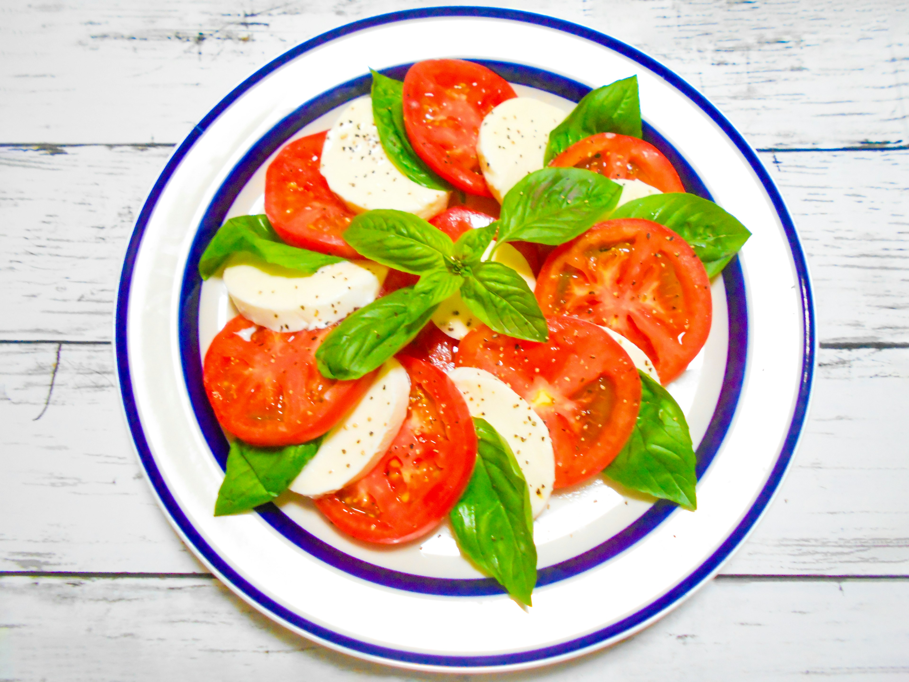 Tomato and mozzarella salad arranged on a blue-rimmed plate garnished with basil leaves