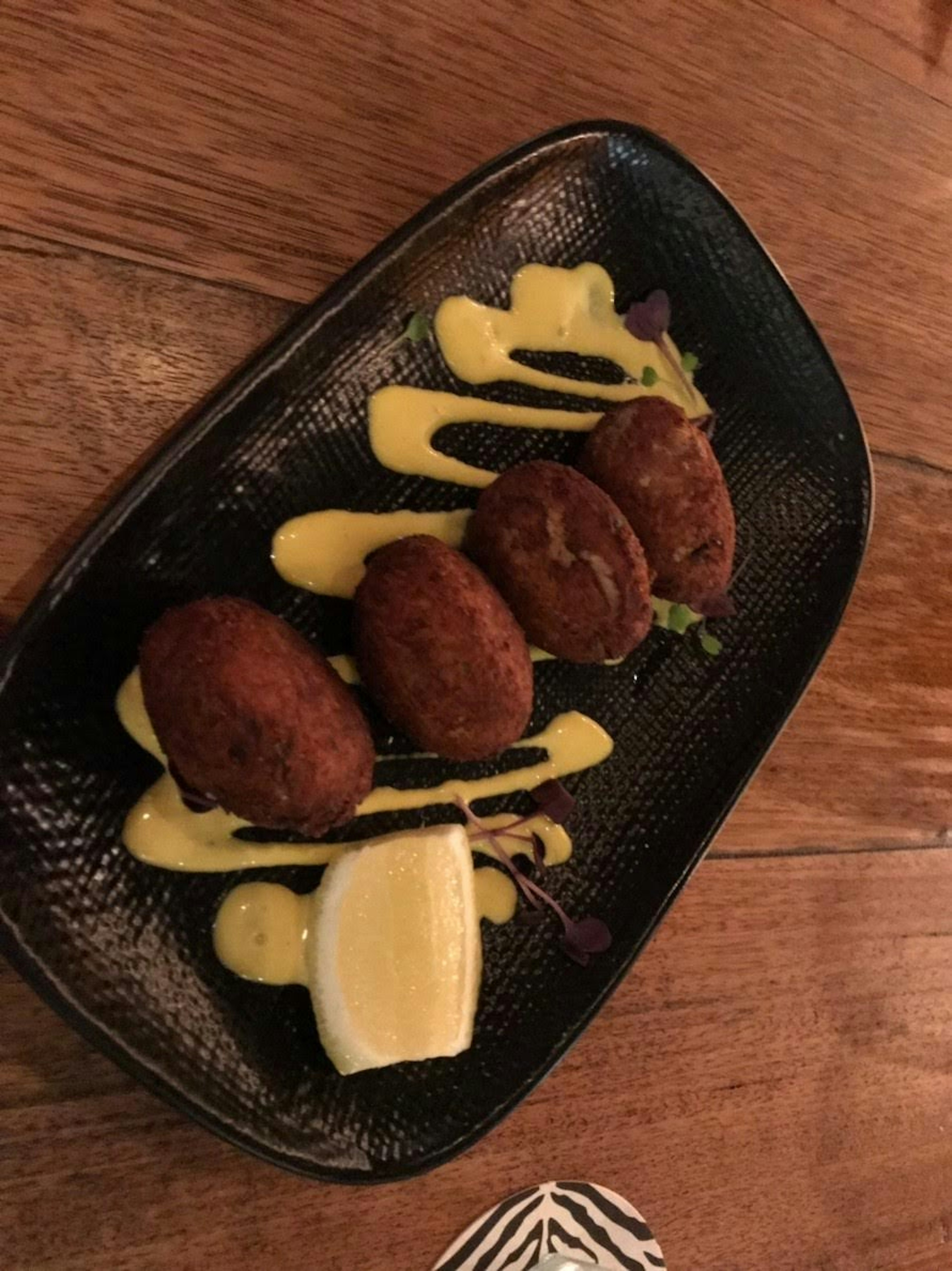 Quatre croquettes disposées sur une assiette noire avec une sauce jaune