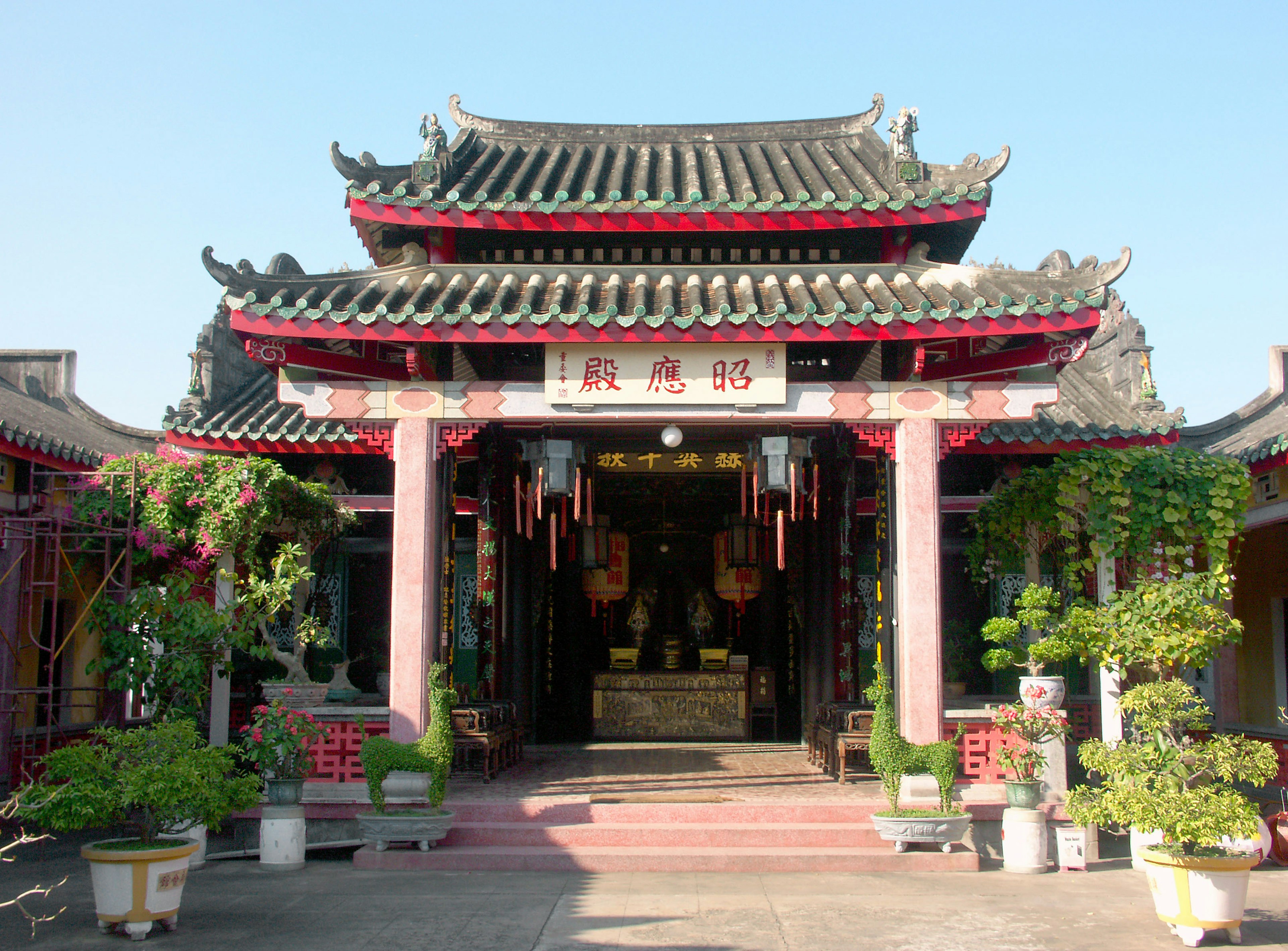 Entrada de un templo de estilo chino con techo intrincado y decoraciones rojas rodeadas de plantas