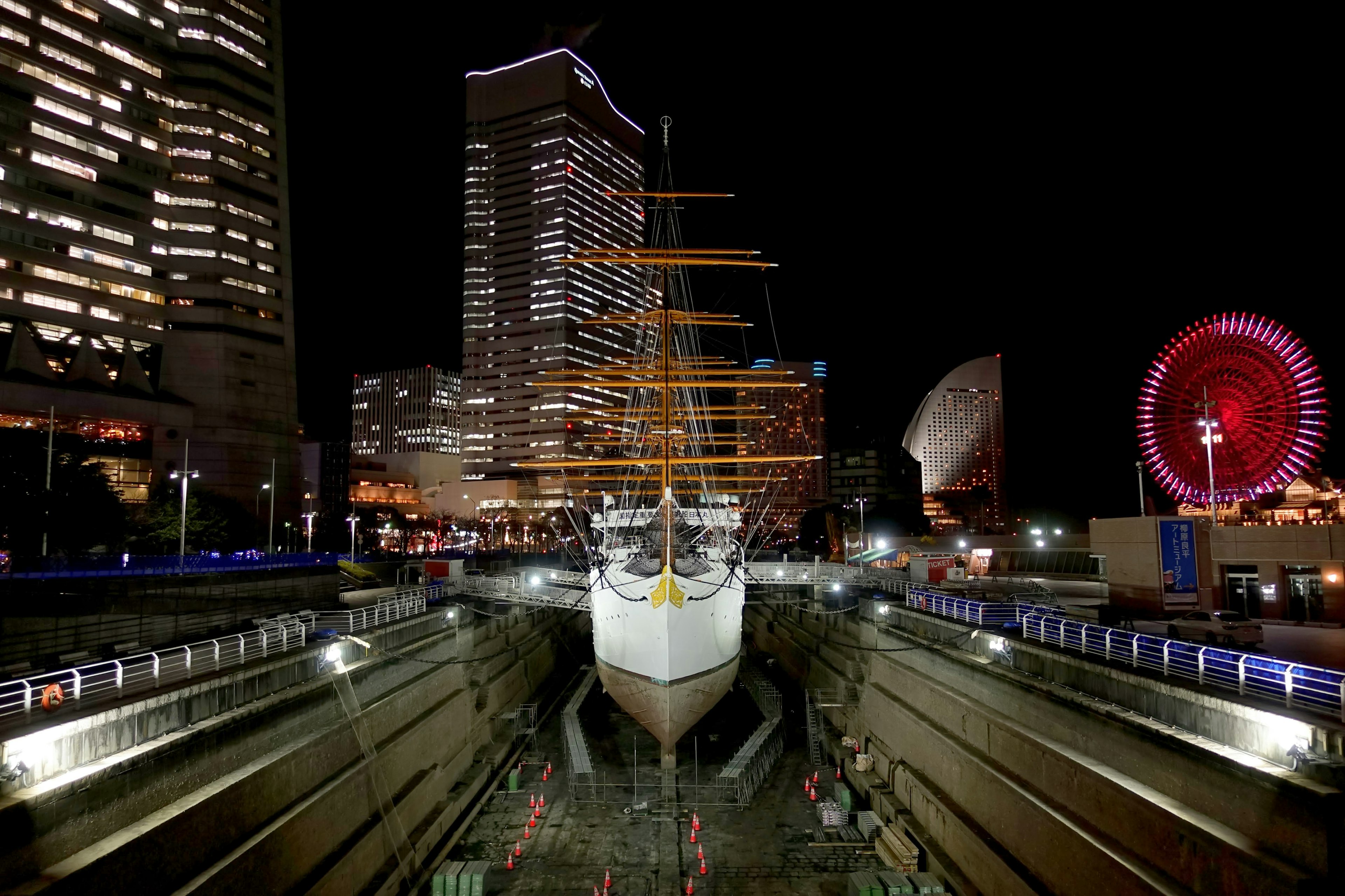 A tall ship illuminated at night with skyscrapers in the background