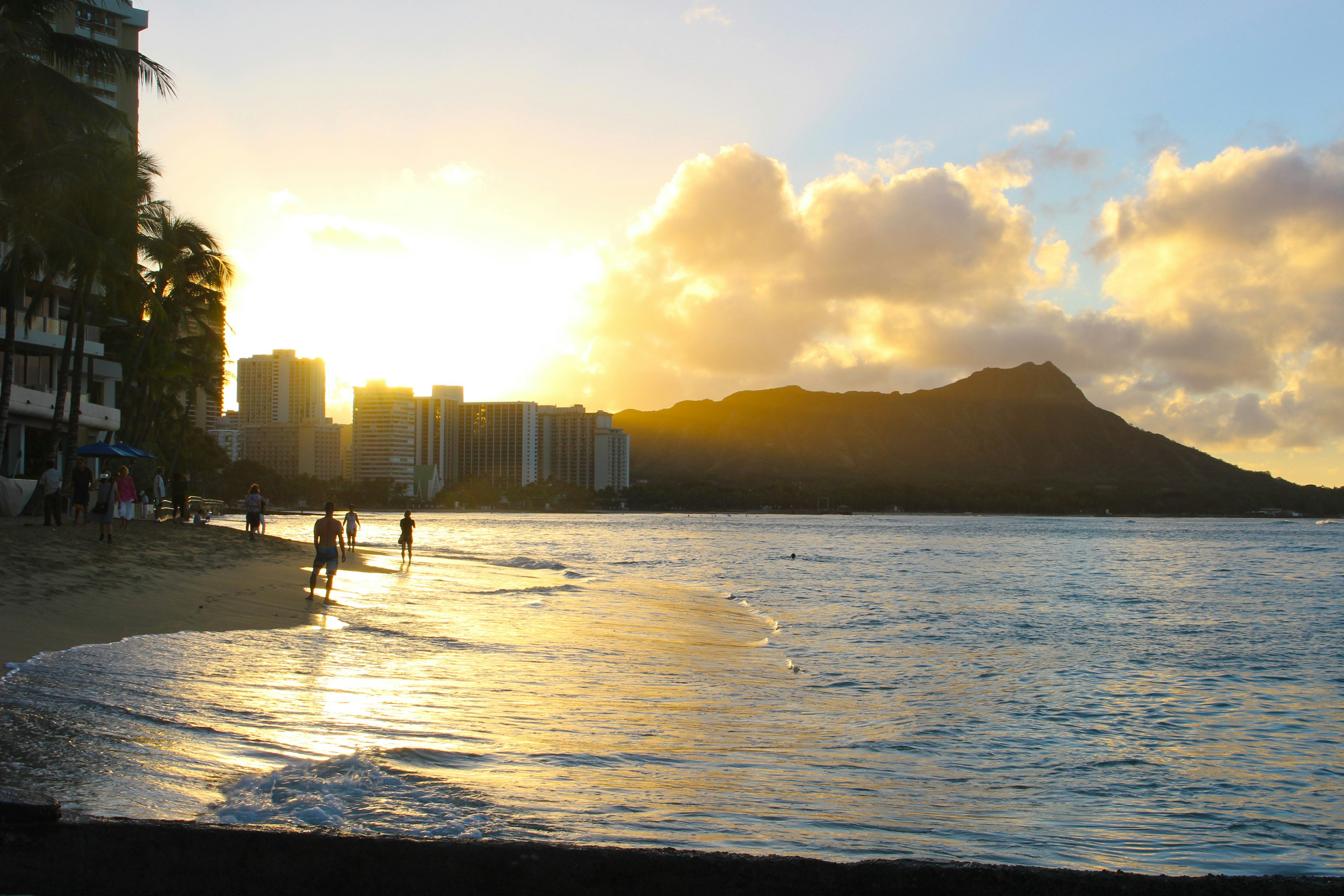 People on a Hawaiian beach at sunset with Diamond Head in the background