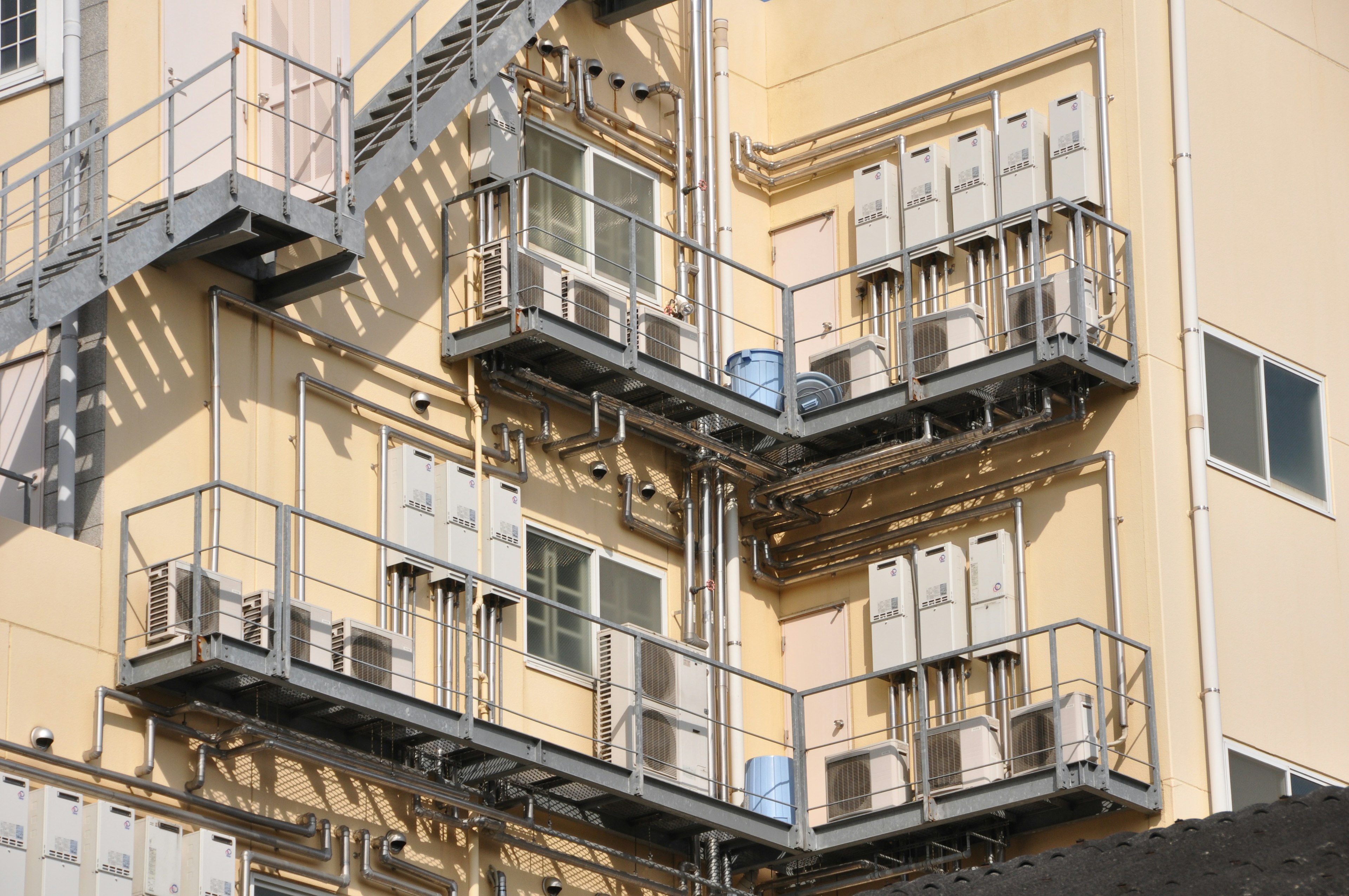 Unidades de aire acondicionado montadas en el exterior de un edificio amarillo con barandillas de metal