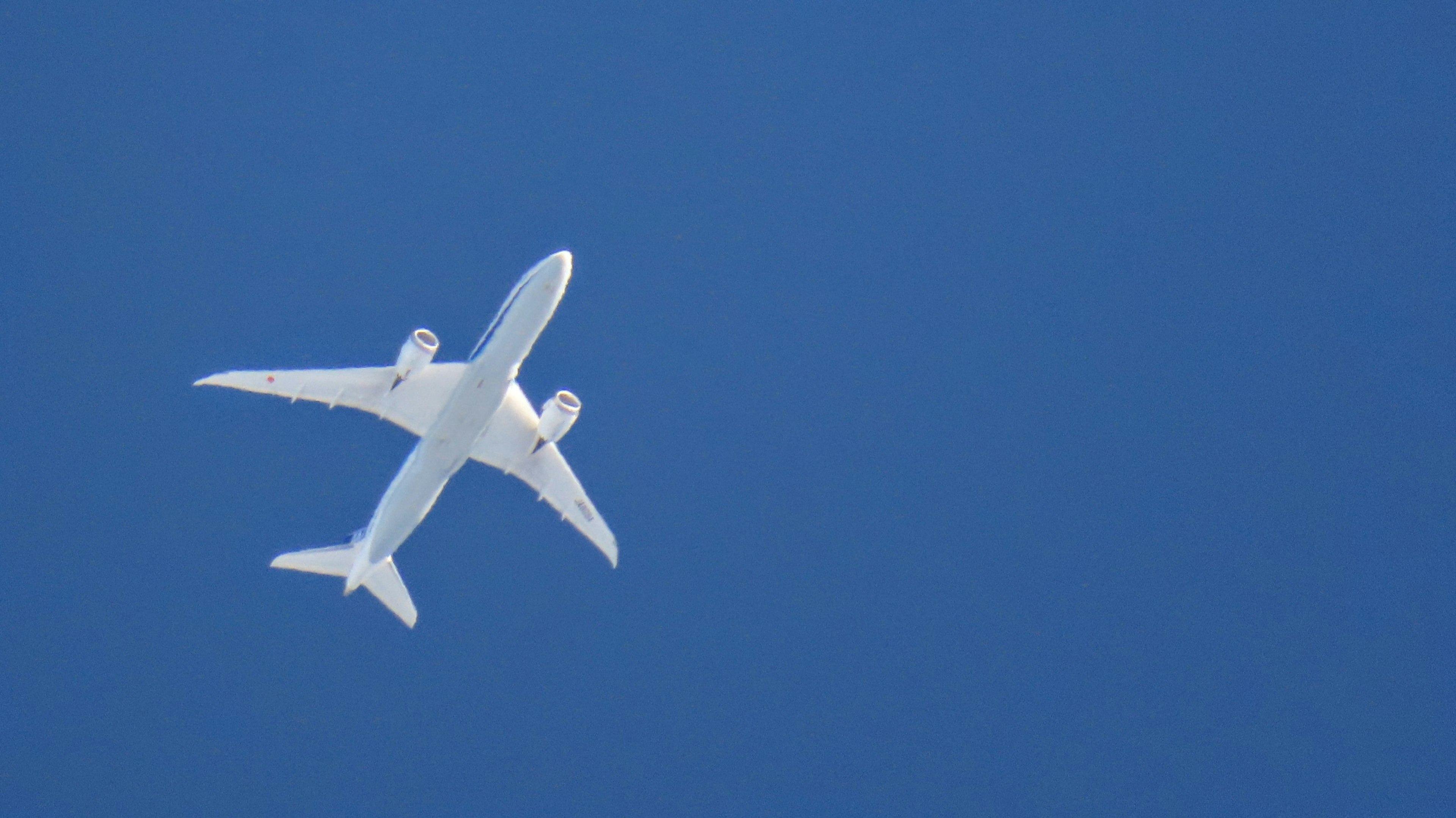 Weißes Flugzeug fliegt in einem klaren blauen Himmel von unten gesehen