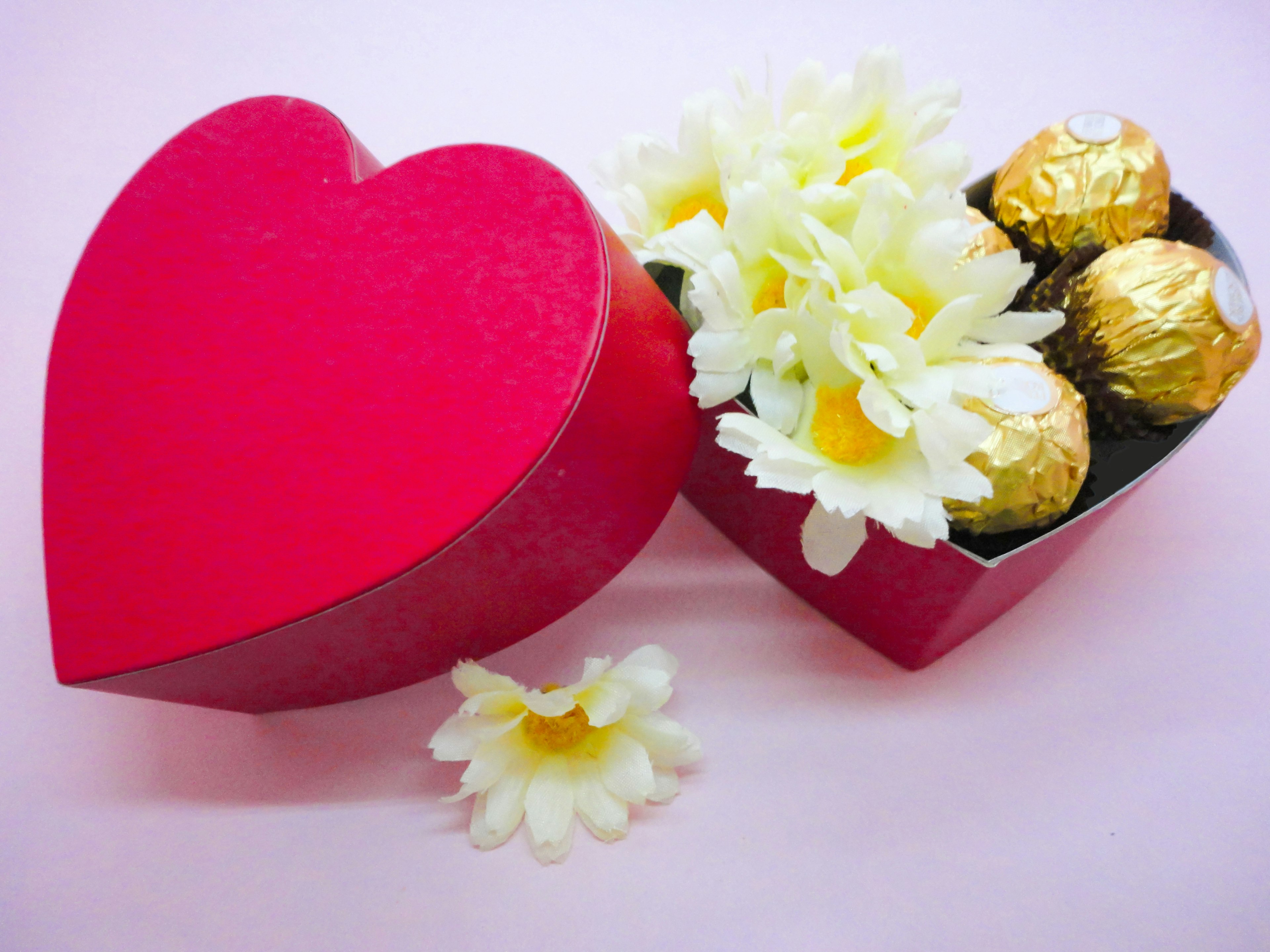 Boîte en forme de cœur rouge avec des fleurs blanches et des chocolats à l'intérieur