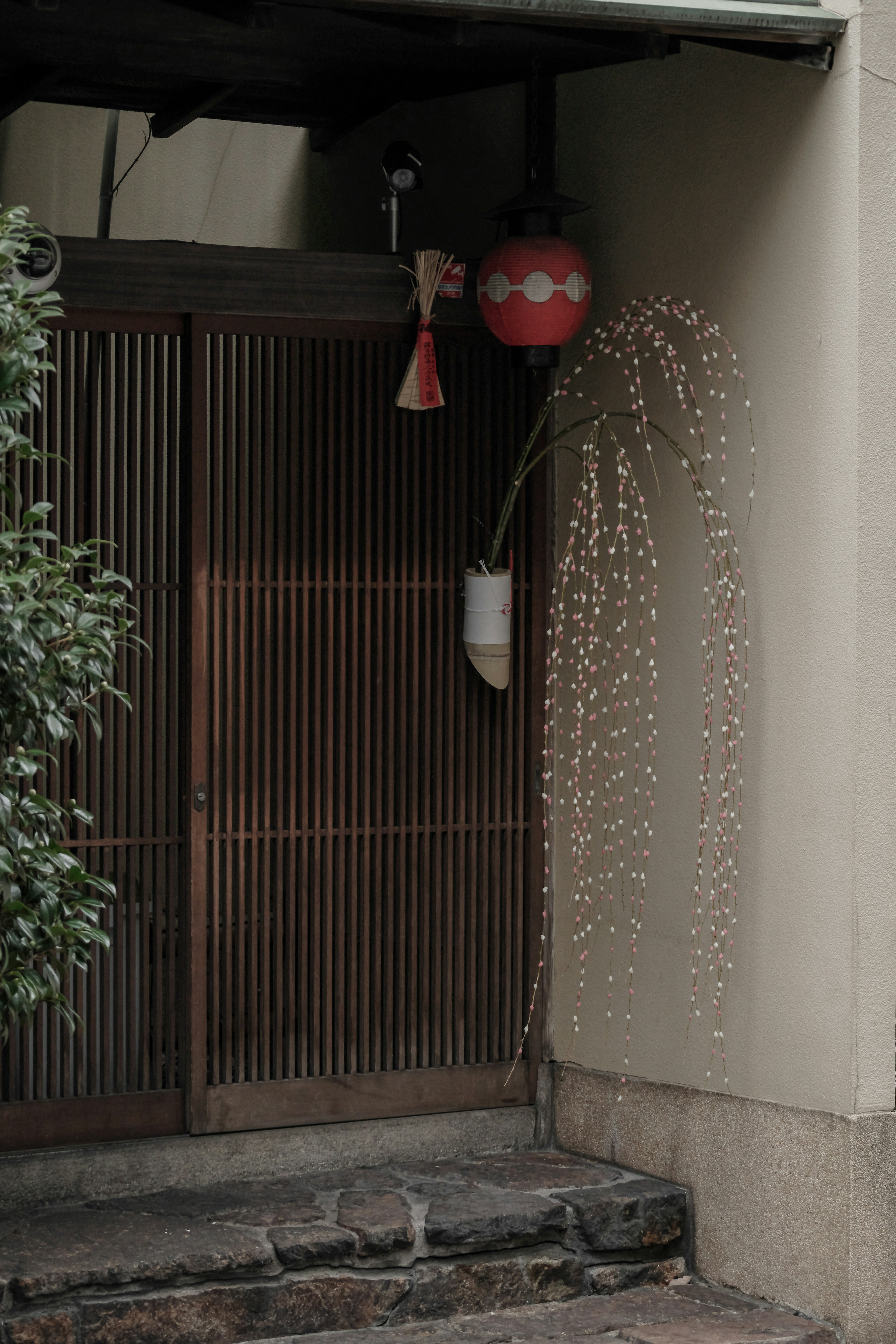 Entrada de casa japonesa tradicional con puerta de madera plantas verdes linterna roja y característica de agua corriente