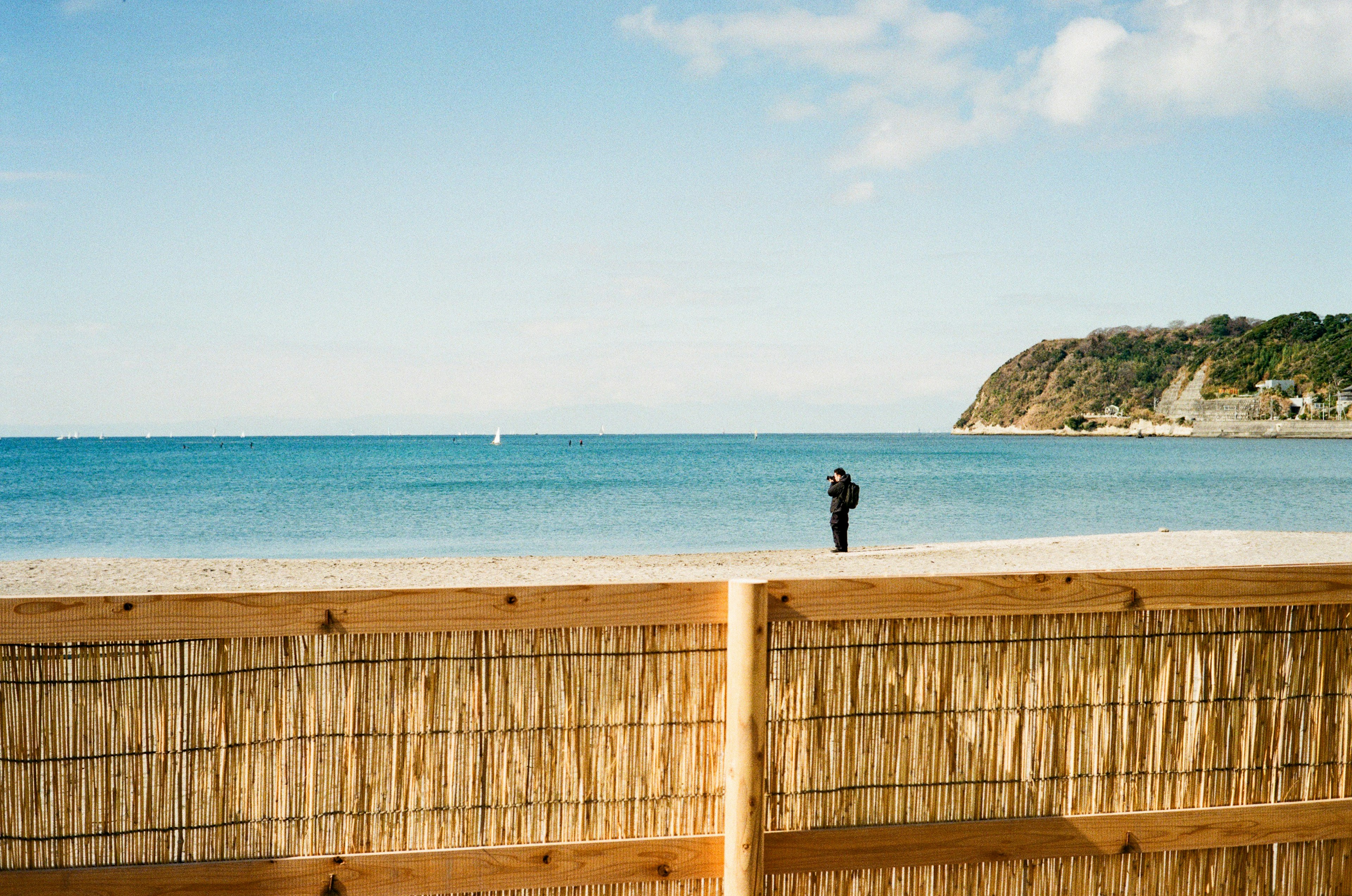 A person standing in front of a wooden fence by the beach with a calm sea