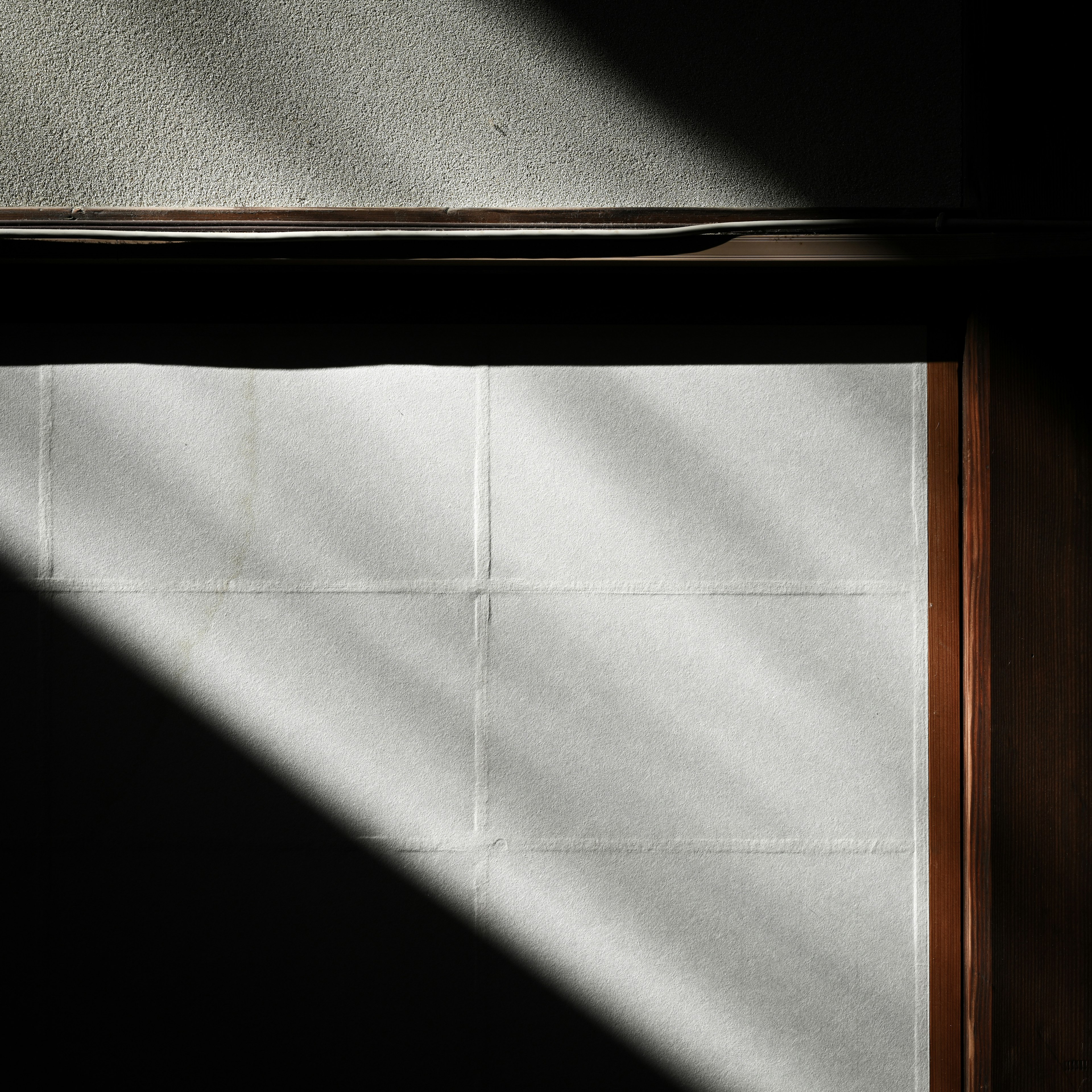 Cornice della finestra in legno che proietta luce e ombra su un muro bianco