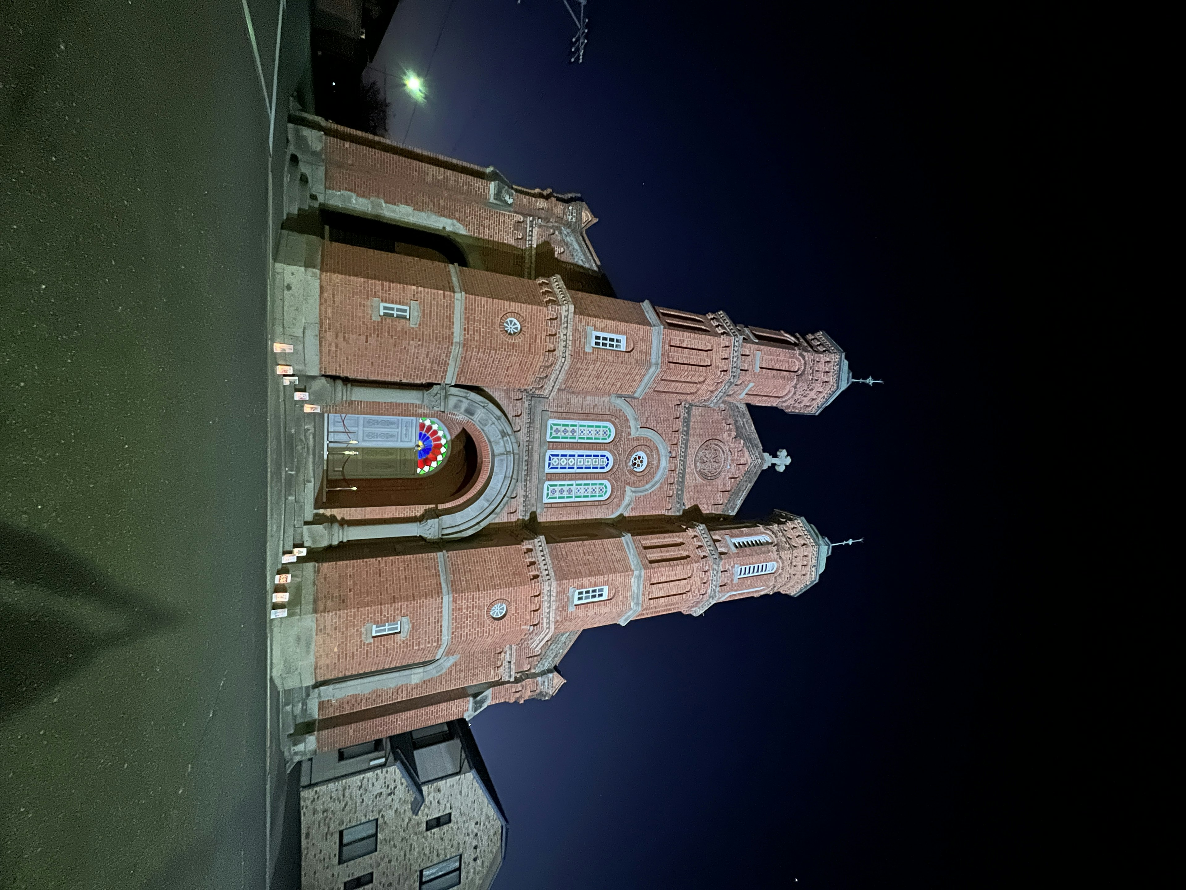 Extérieur d'une église rouge la nuit avec de grandes tours et une entrée décorative