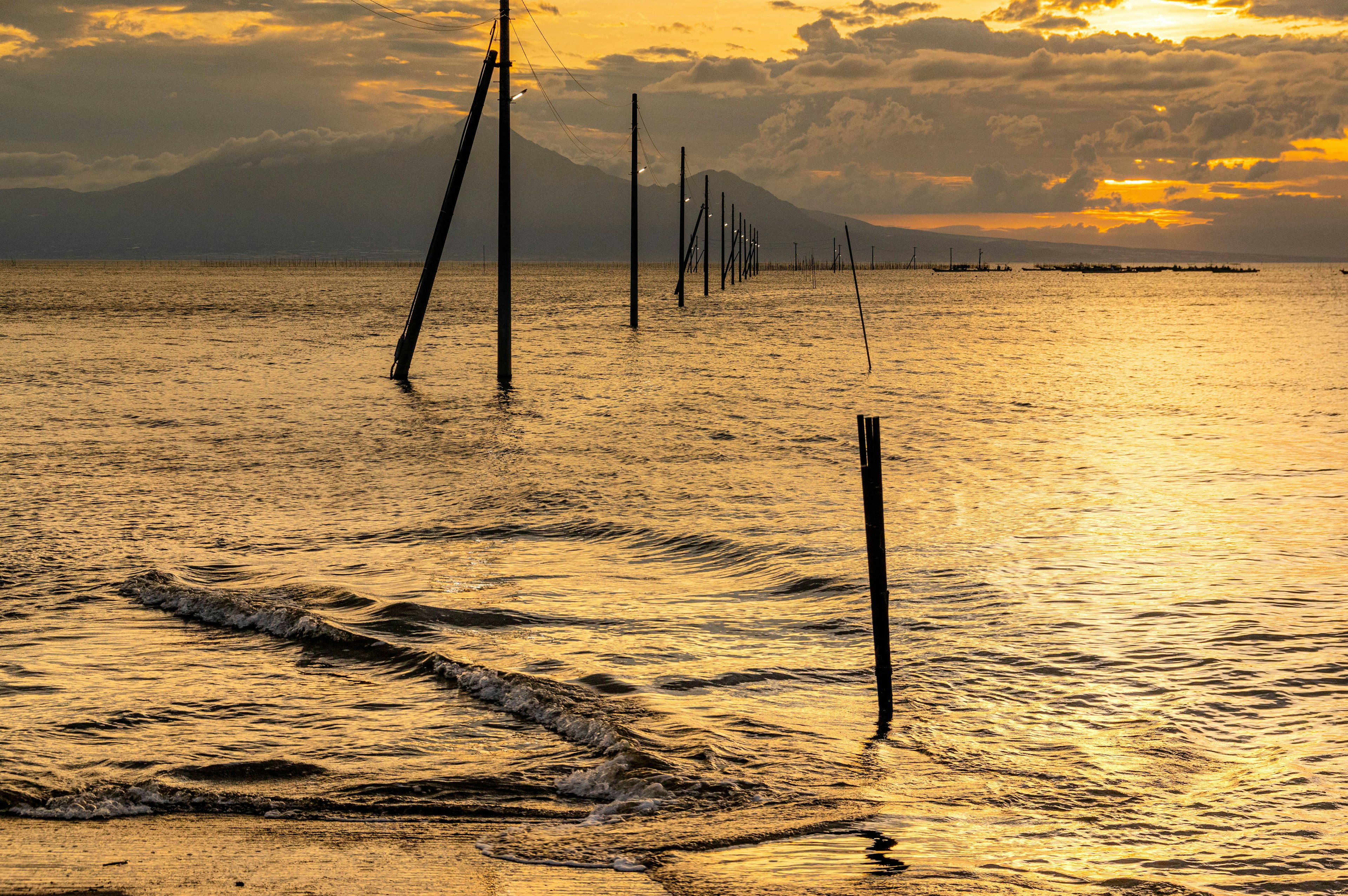 Holzpfeiler stehen im Meer bei Sonnenuntergang mit sanften Wellen