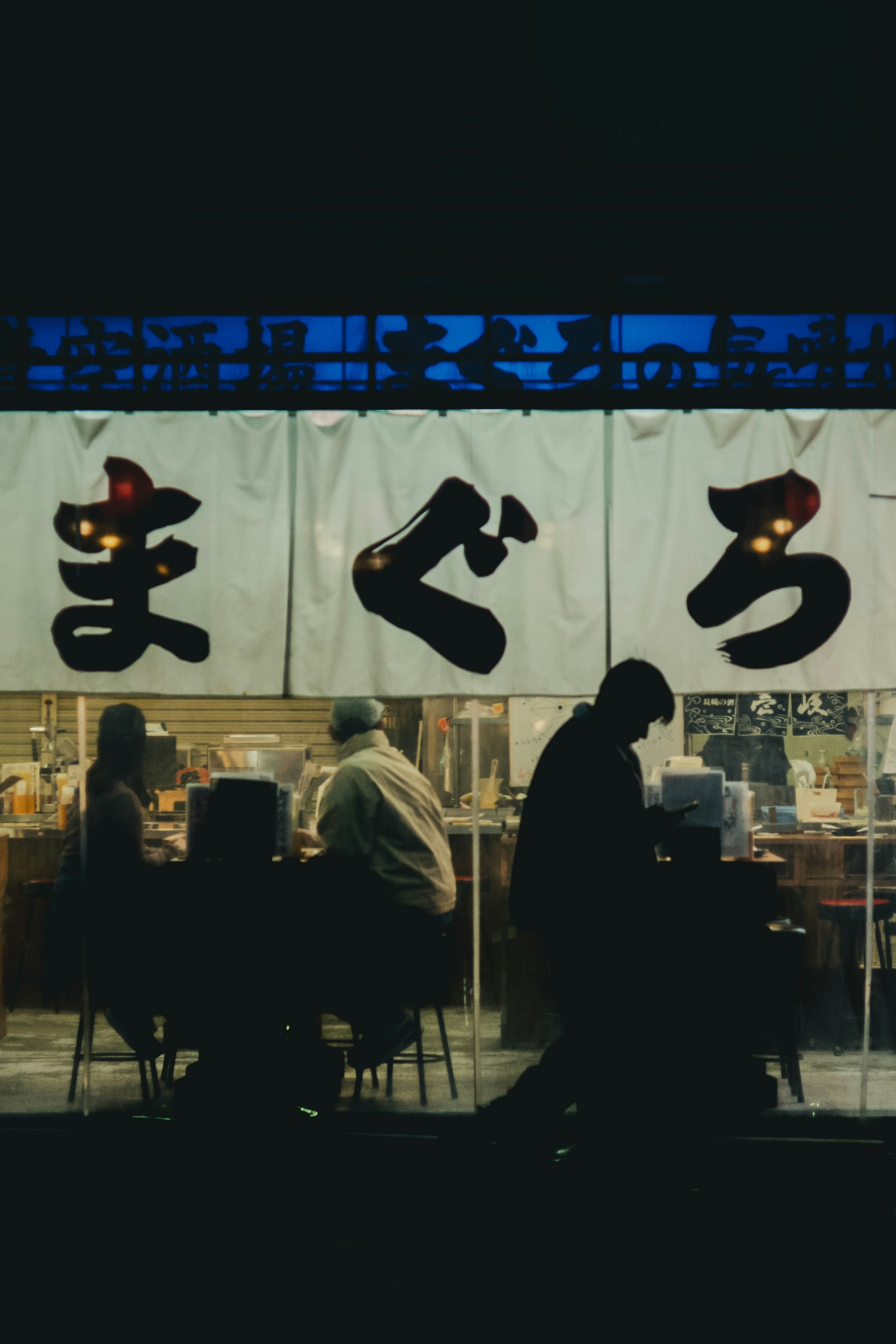 Silhouettes de personnes assises devant un izakaya avec une enseigne en japonais