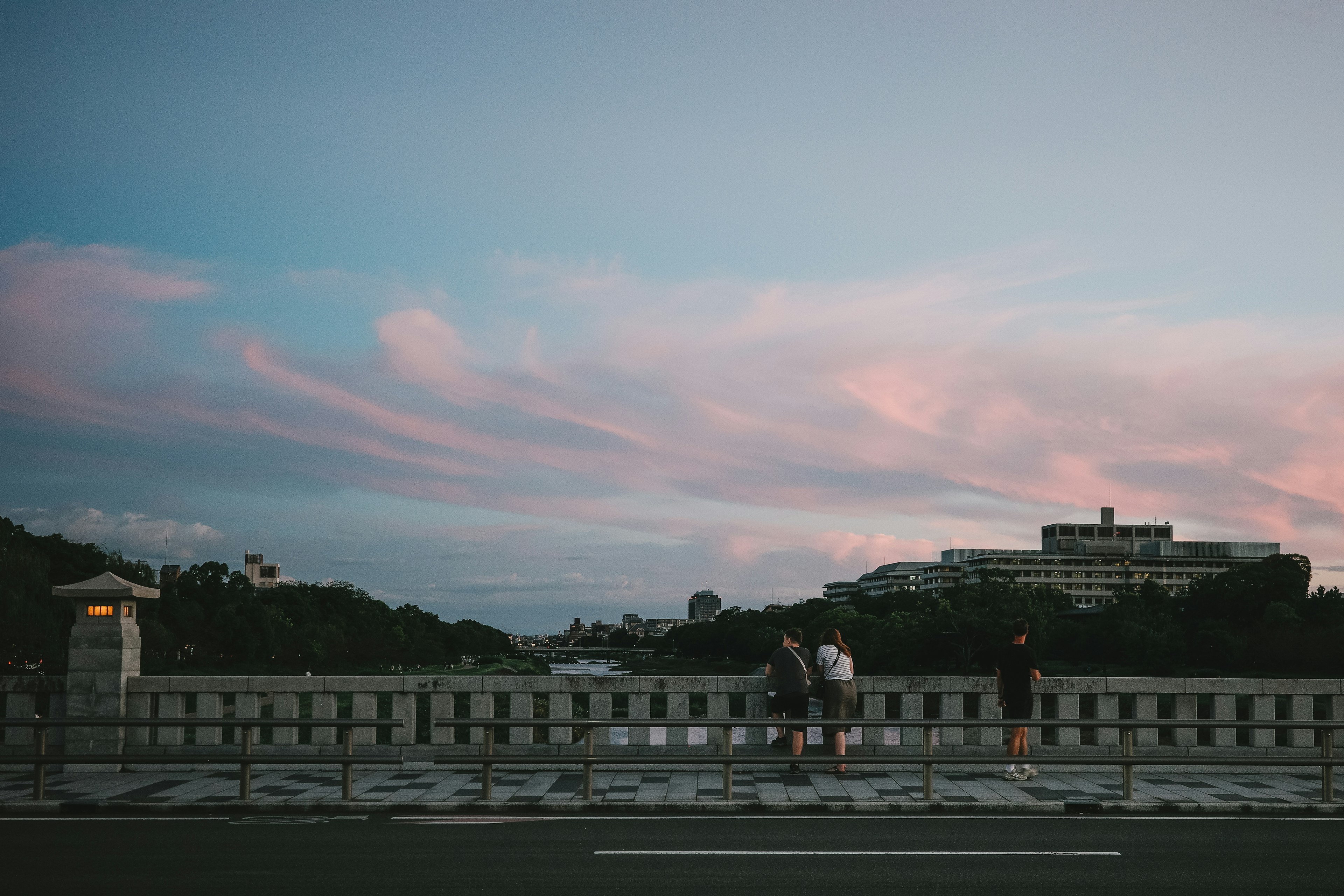 夕暮れの空に浮かぶピンクの雲と橋の上に立つ人々