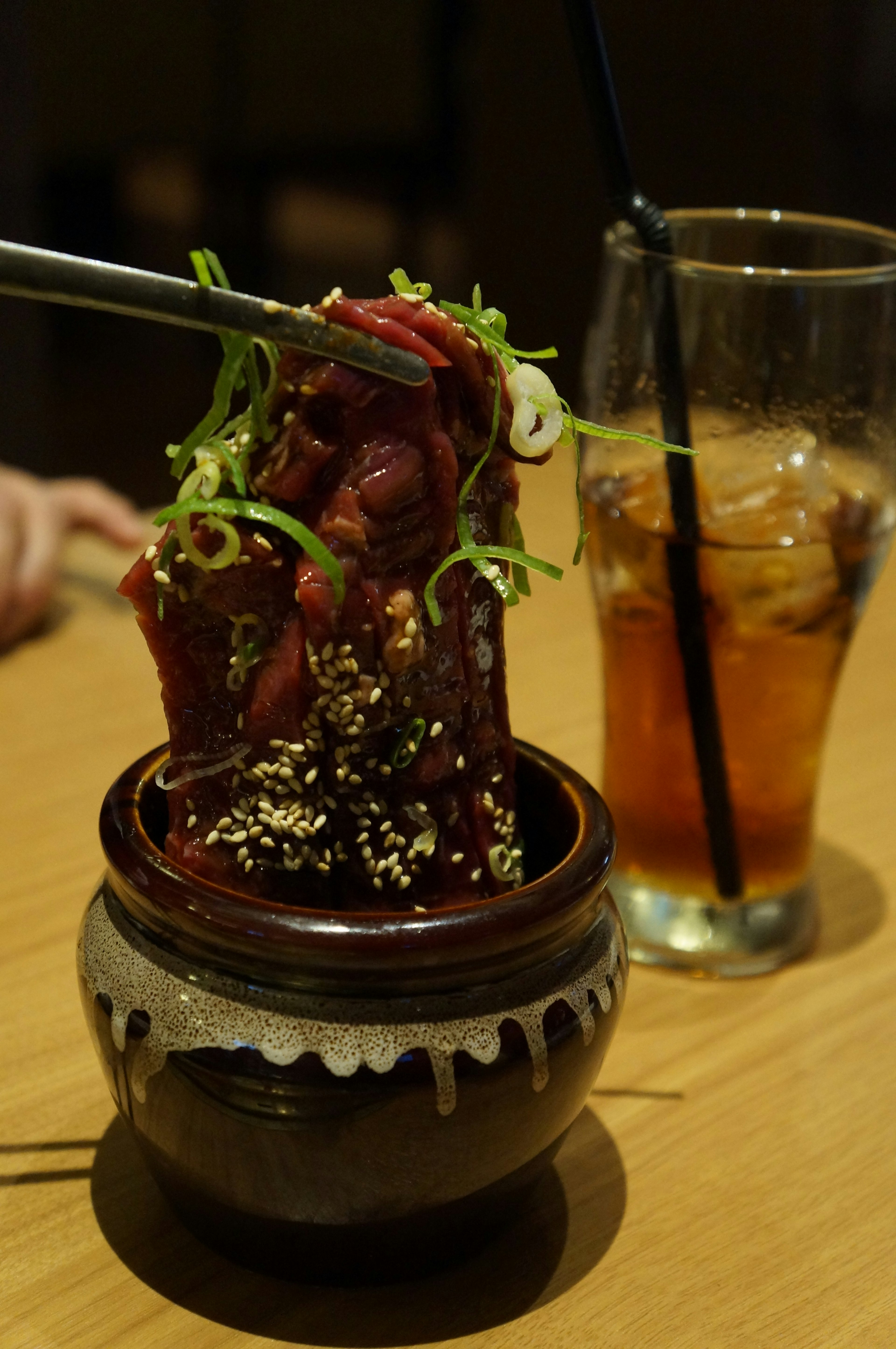 Un plato de carne delicioso decorado con cebollas verdes y sésamo en una pequeña olla con una bebida