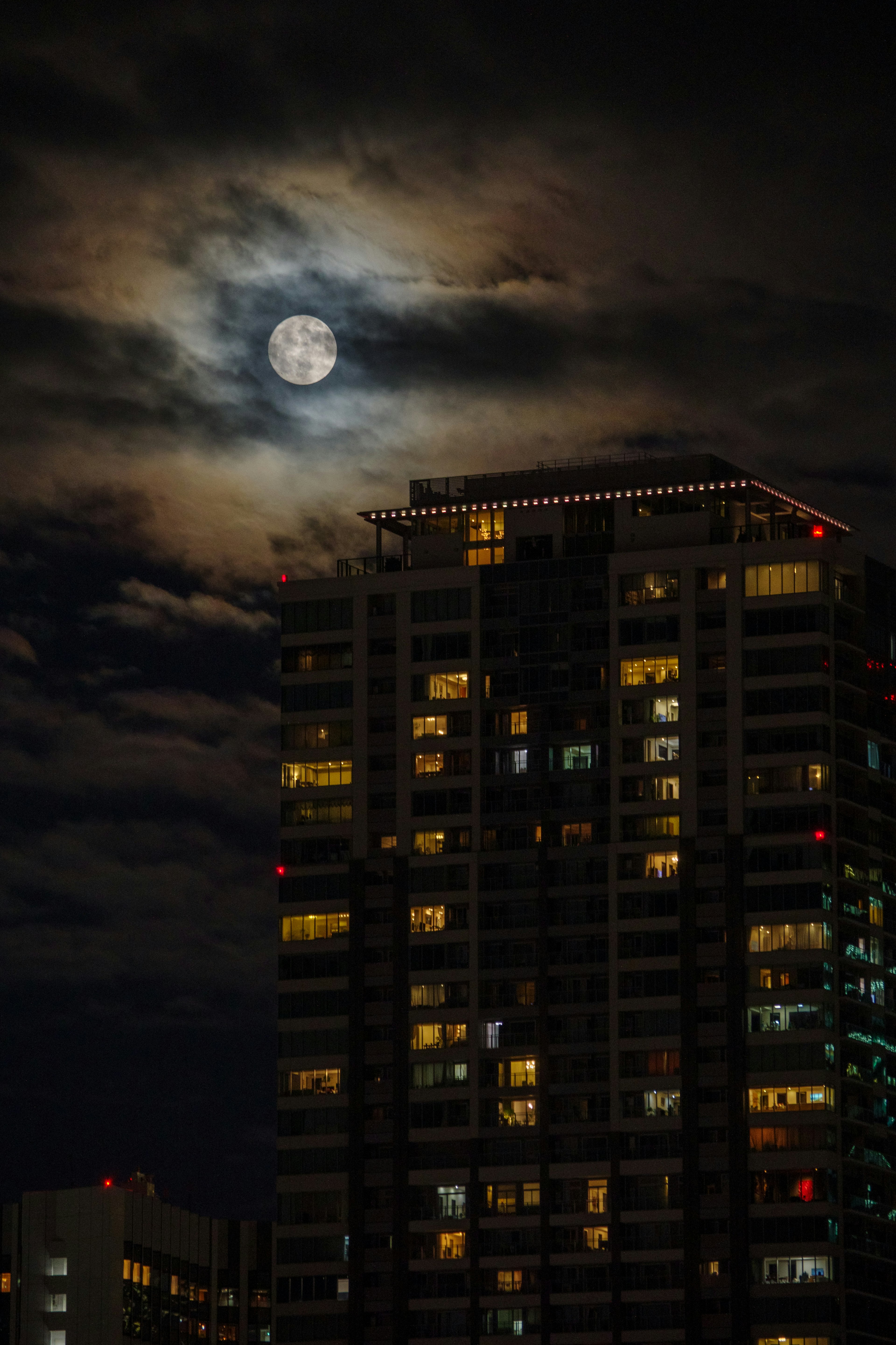 Bulan purnama di langit malam di atas gedung pencakar langit dengan jendela yang menyala