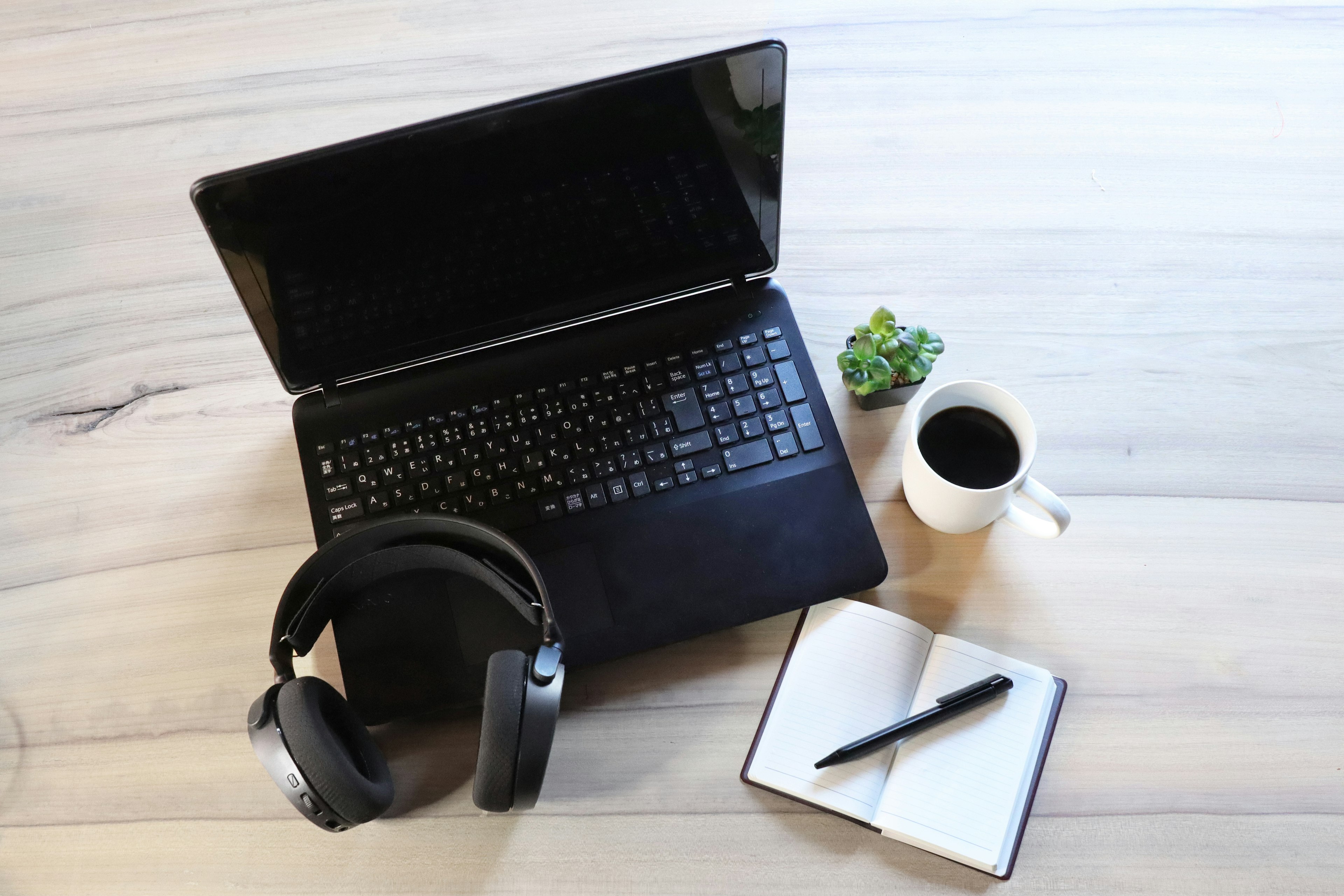 laptop hitam dengan headphone cangkir kopi dan buku catatan di meja