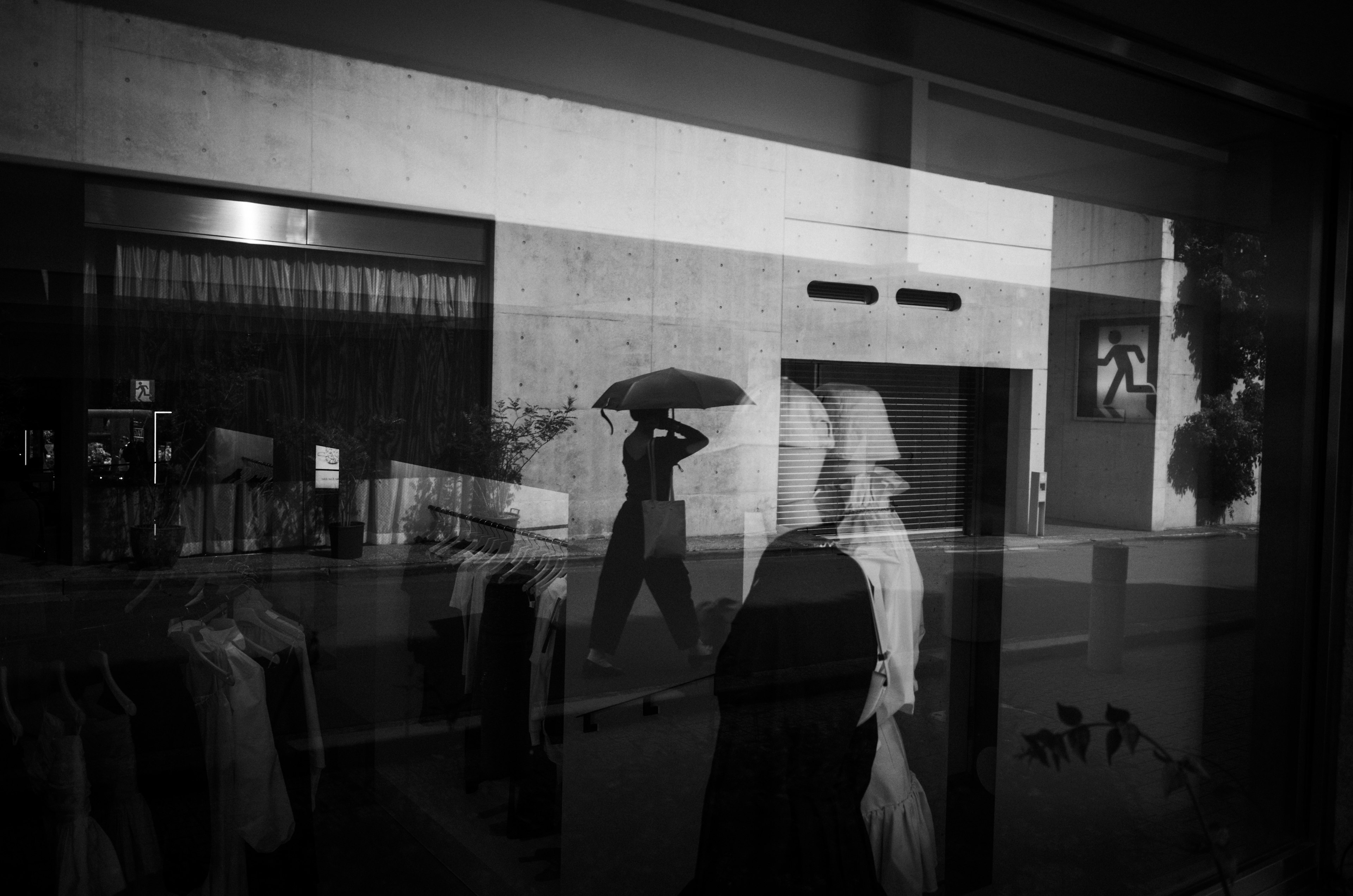 Scène de rue en noir et blanc avec une personne tenant un parapluie et des figures réfléchies