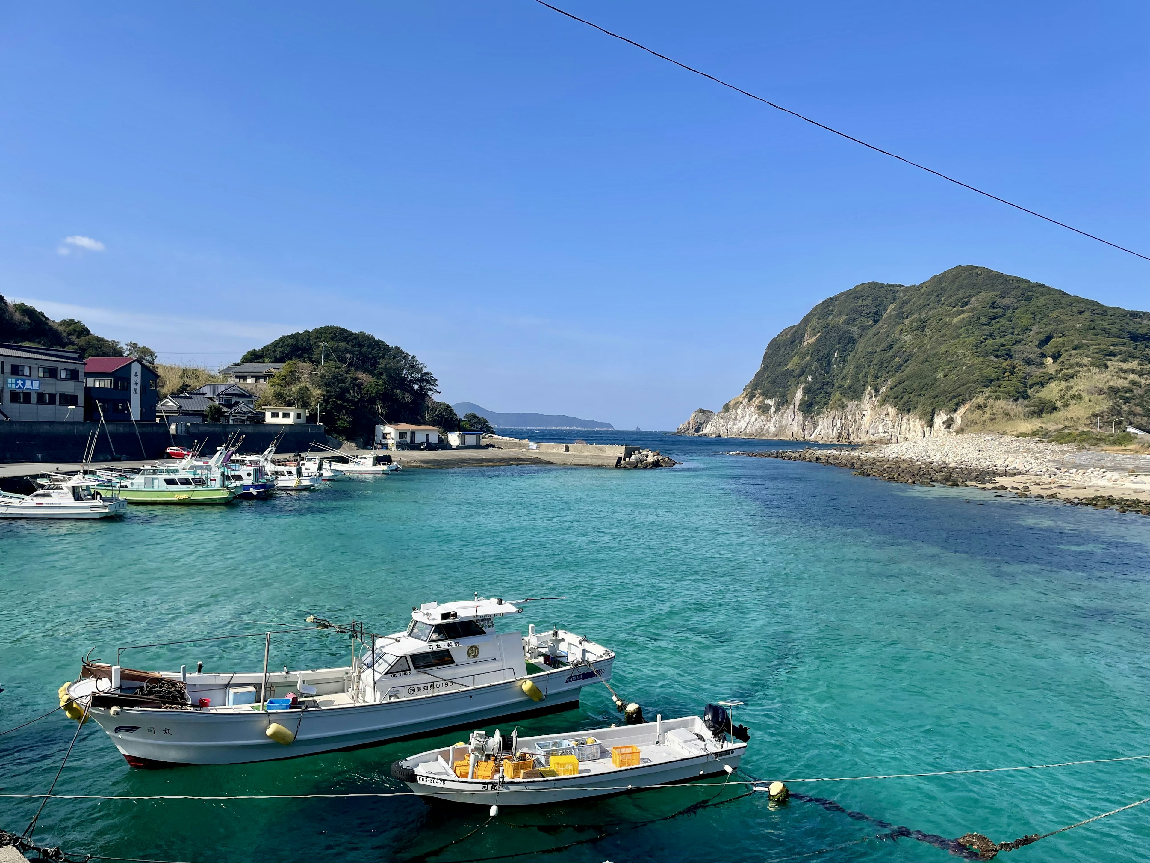 青い海と小さな漁船が浮かぶ港の風景