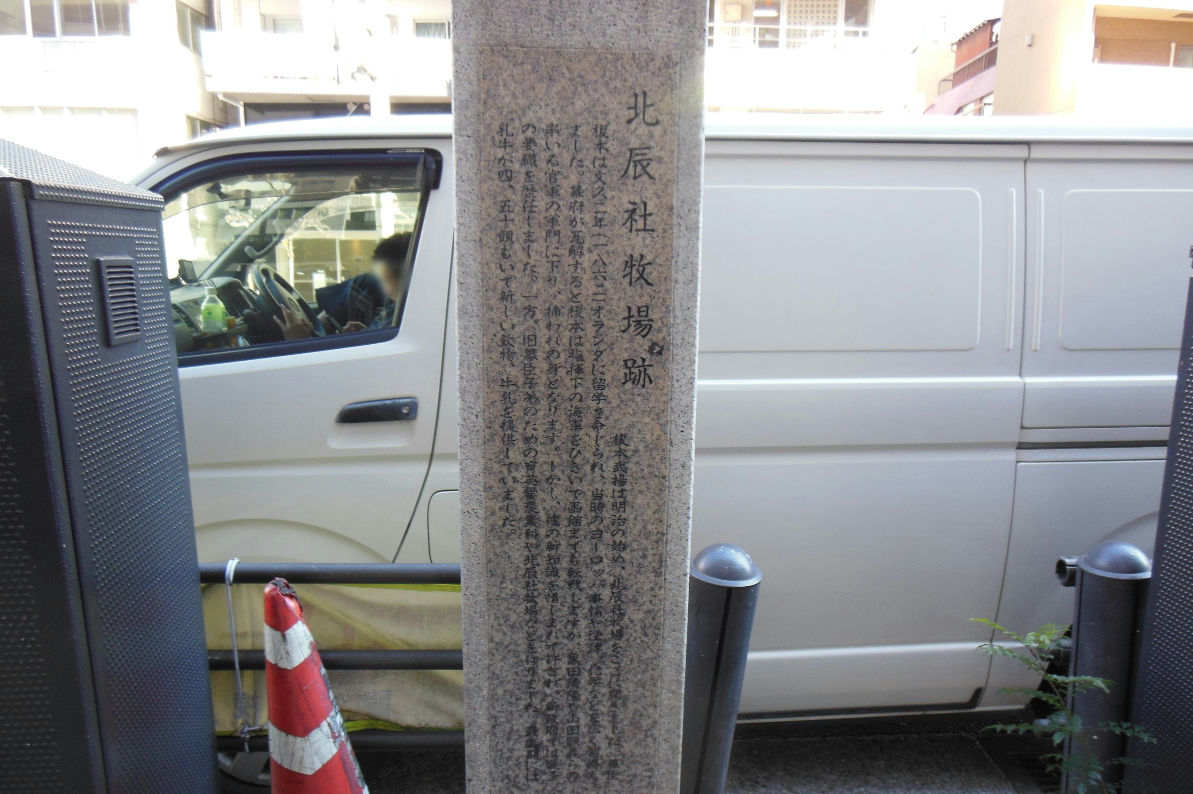 Monumento de piedra al lado de una furgoneta blanca con inscripciones en japonés