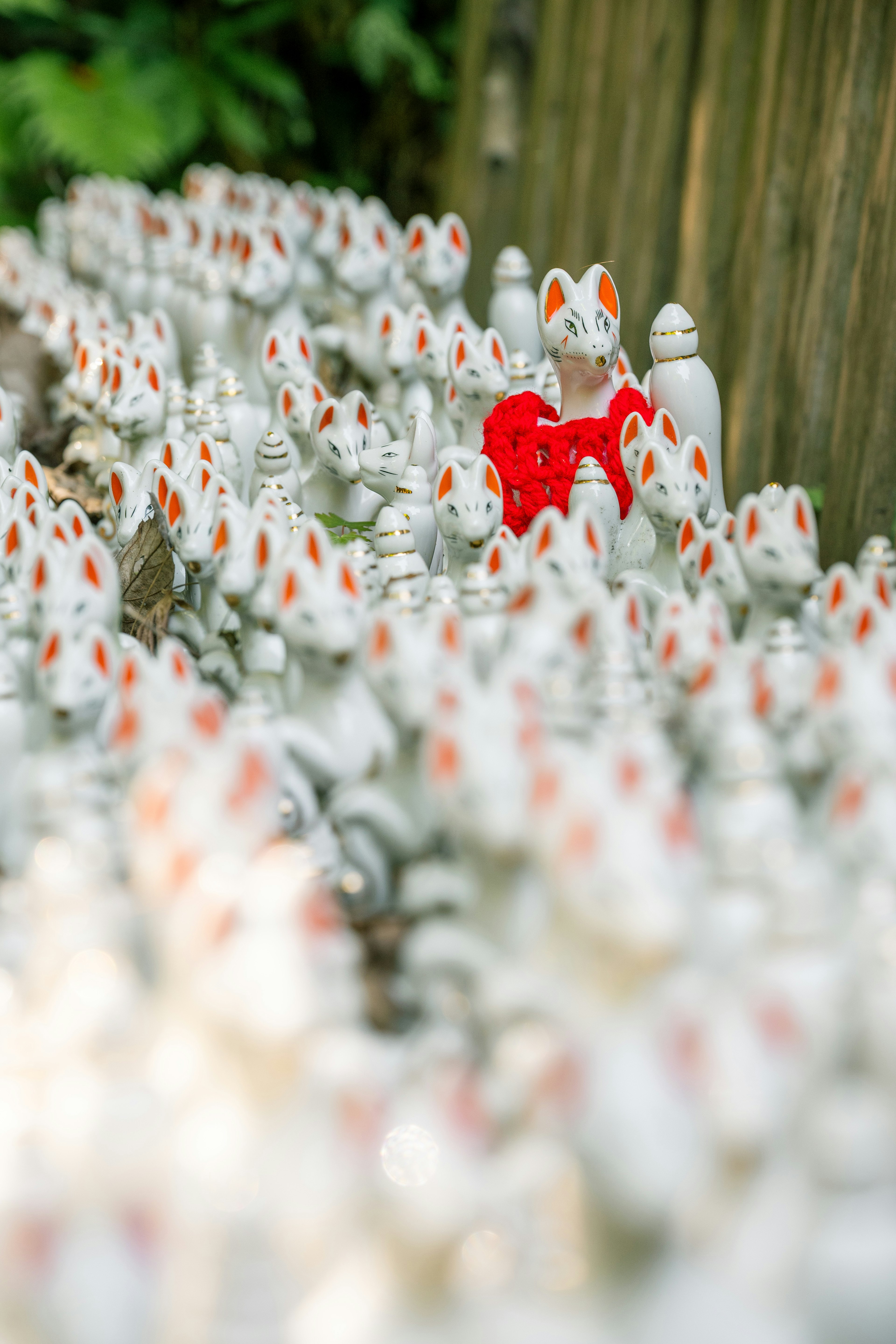 Une statue de renard vêtue de rouge parmi une multitude de statues de renards blancs