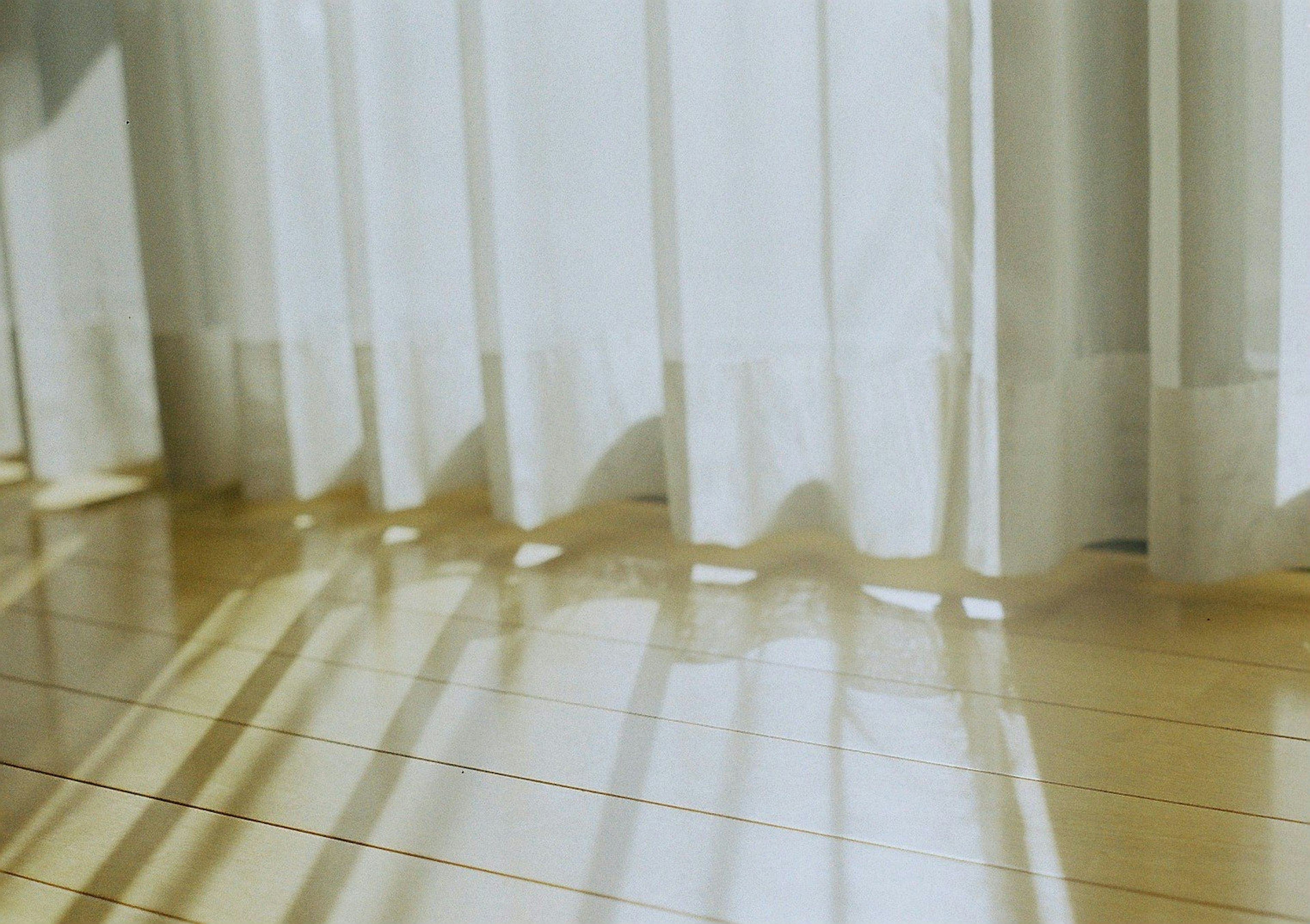 Sheer curtains allowing light to filter through casting shadows on the floor