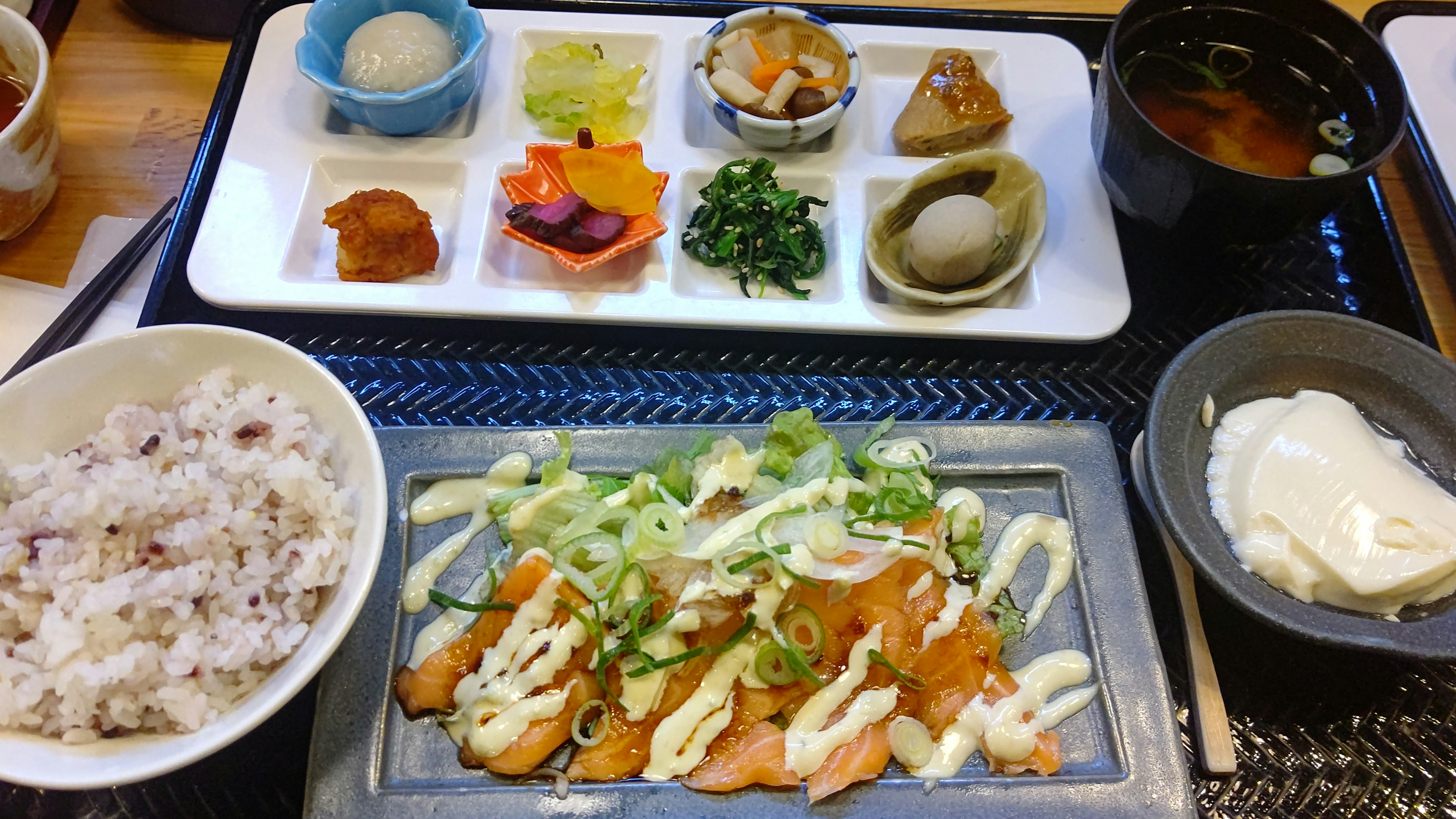 Japanese meal set featuring salmon with green onions, brown rice, miso soup, and various side dishes